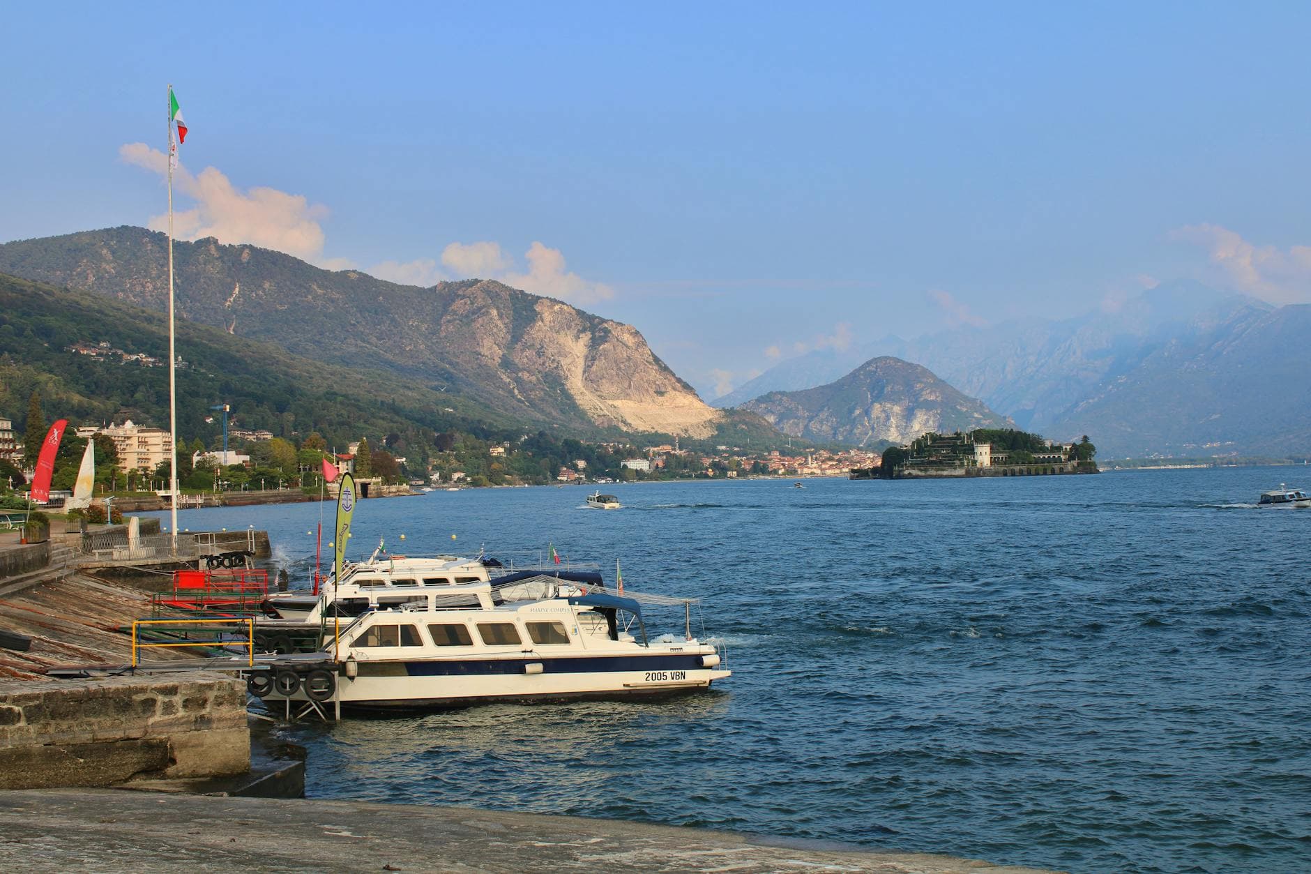 Beautiful view of Lake Maggiore with boats docked, scenic mountains, and coastline in Stresa, Italy.