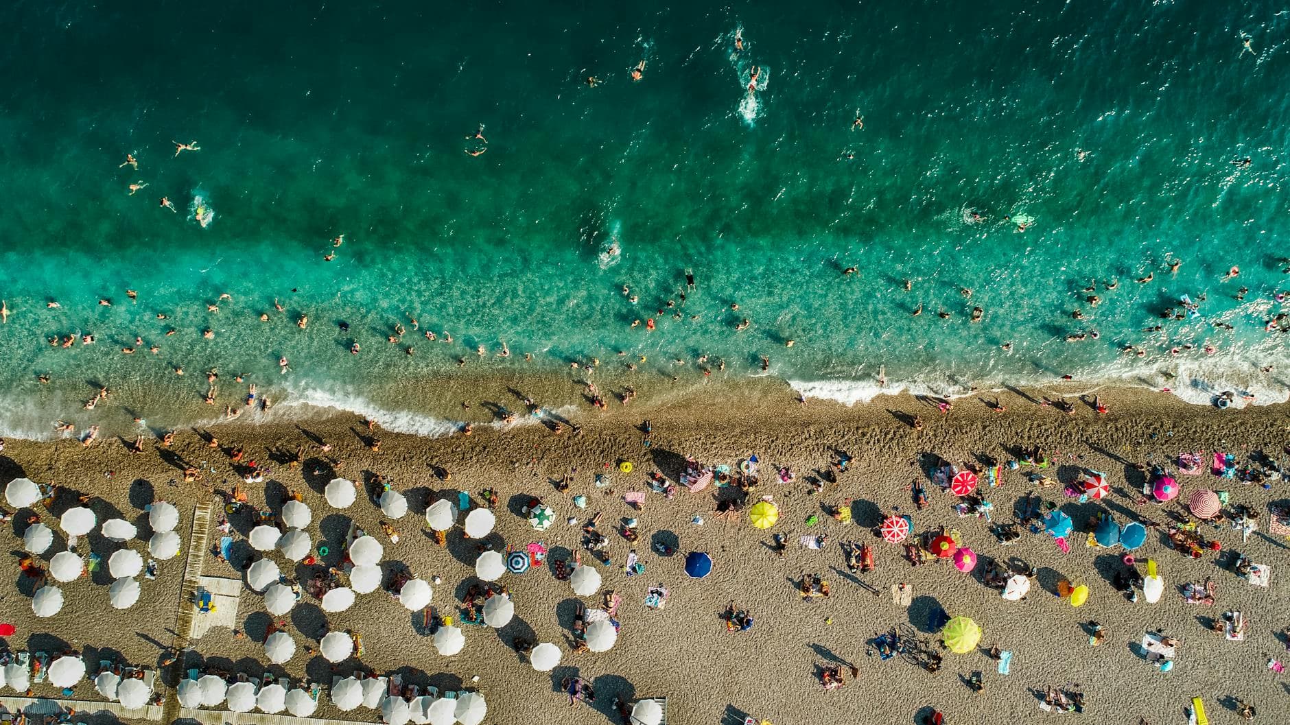 Vibrant summer scene on Antalya's Konyaalti Beach with turquoise waters and colorful umbrellas.