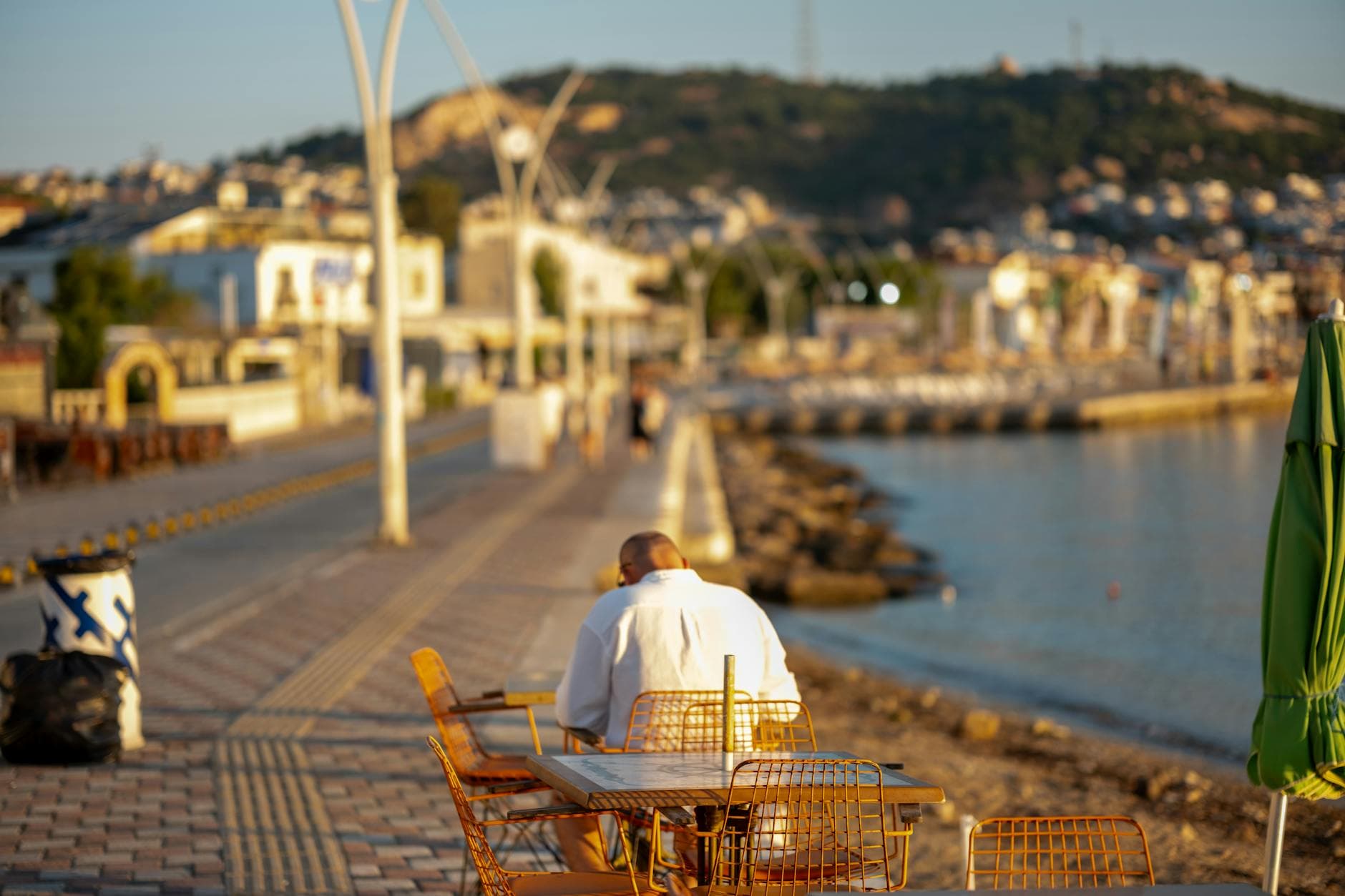 Peaceful seaside view of a man sitting on a promenade table in Yenifoca, İzmir, Turkey.