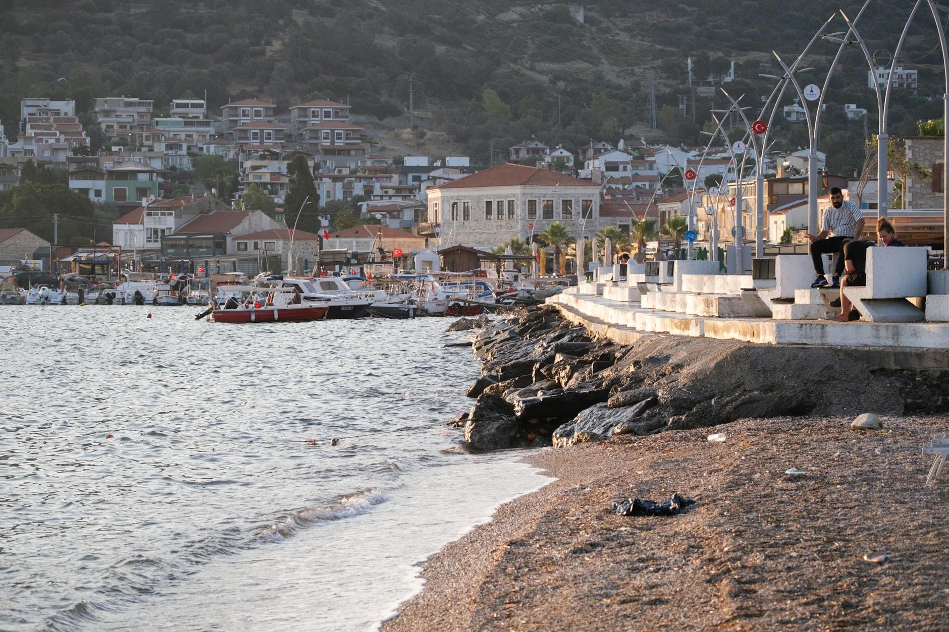 Peaceful seaside view of Foça, İzmir, Turkey with boats and promenade at sunset.