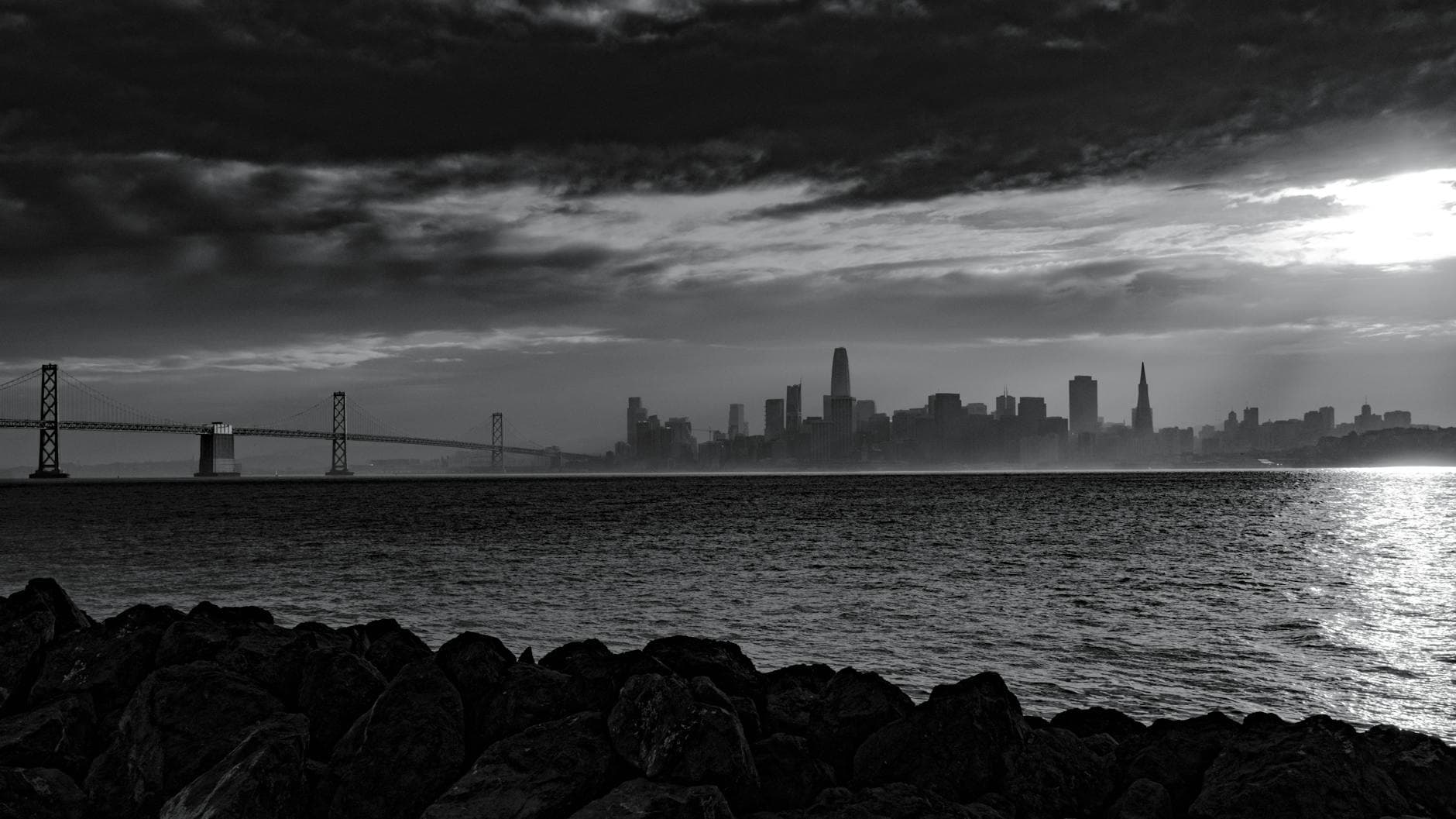 A dramatic black and white view of the San Francisco skyline with the Bay Bridge at sunrise.