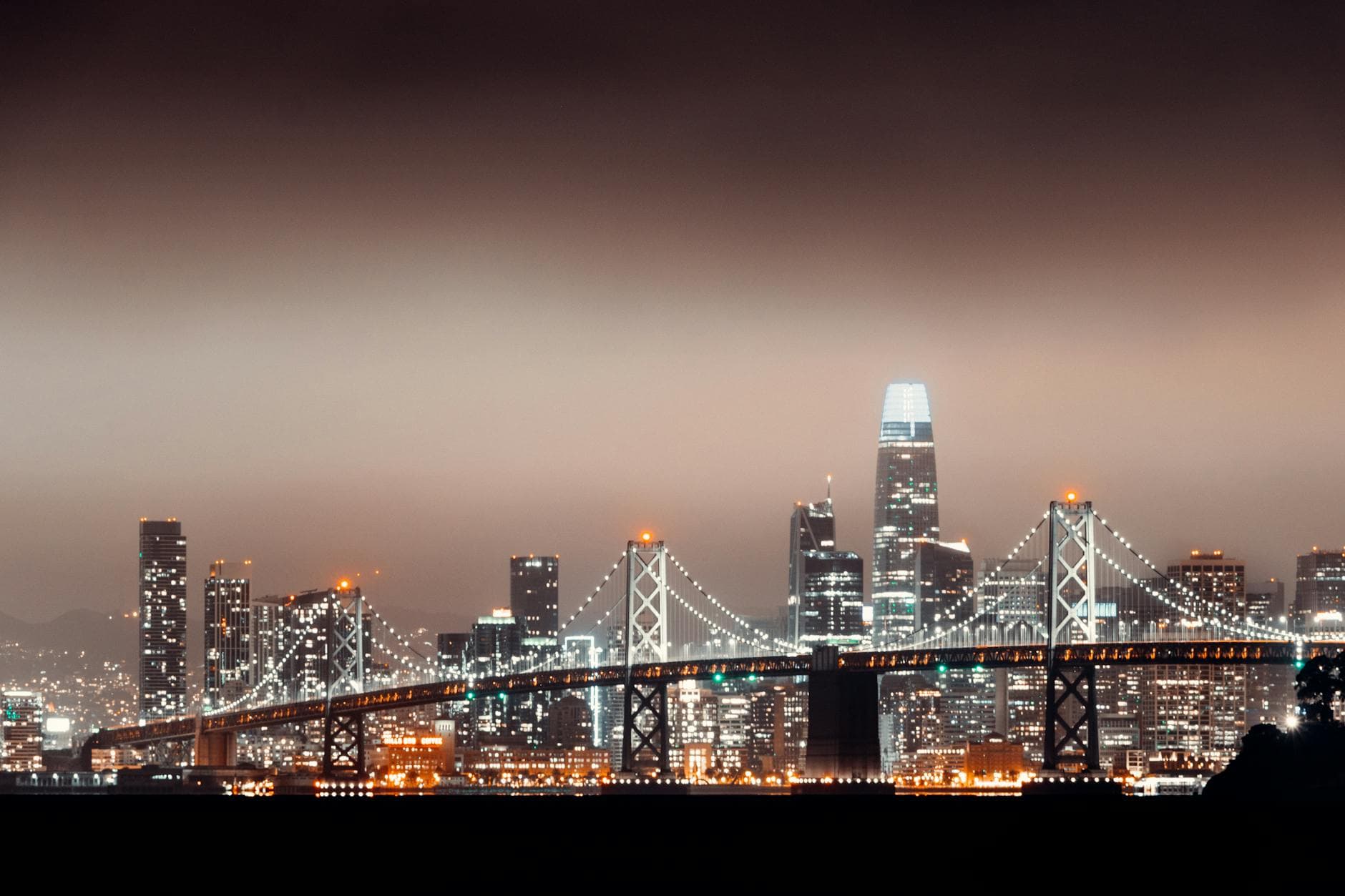 Night view of San Francisco skyline and Bay Bridge illuminated with city lights.