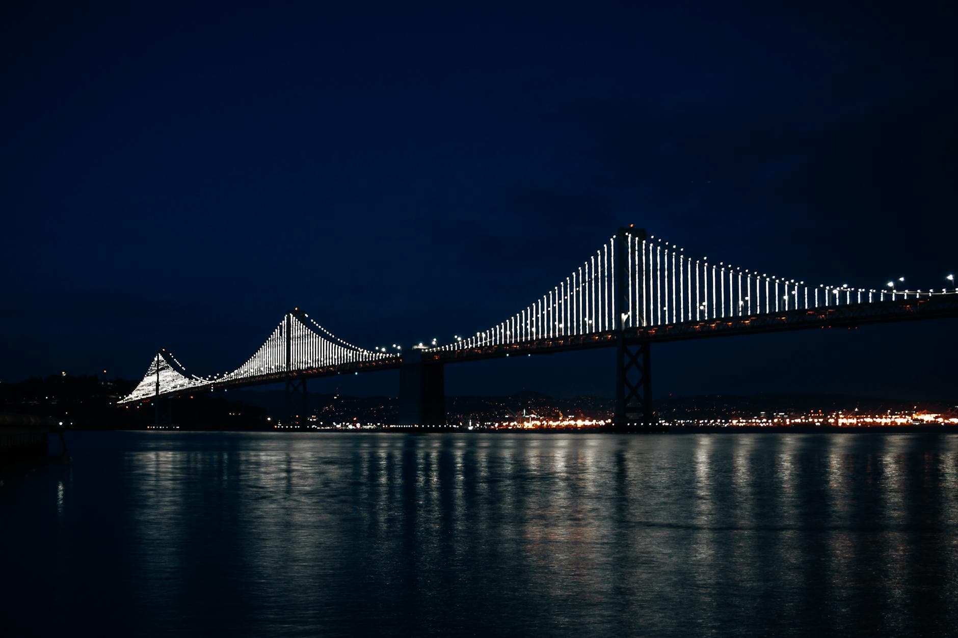 Breathtaking view of the Bay Bridge illuminated against the night sky reflecting over the water.