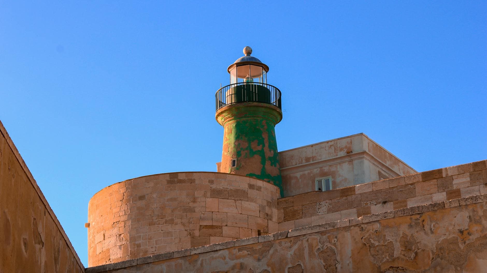 A striking view of a traditional lighthouse in the historic town of Siracusa, Sicily, against a clear blue sky.