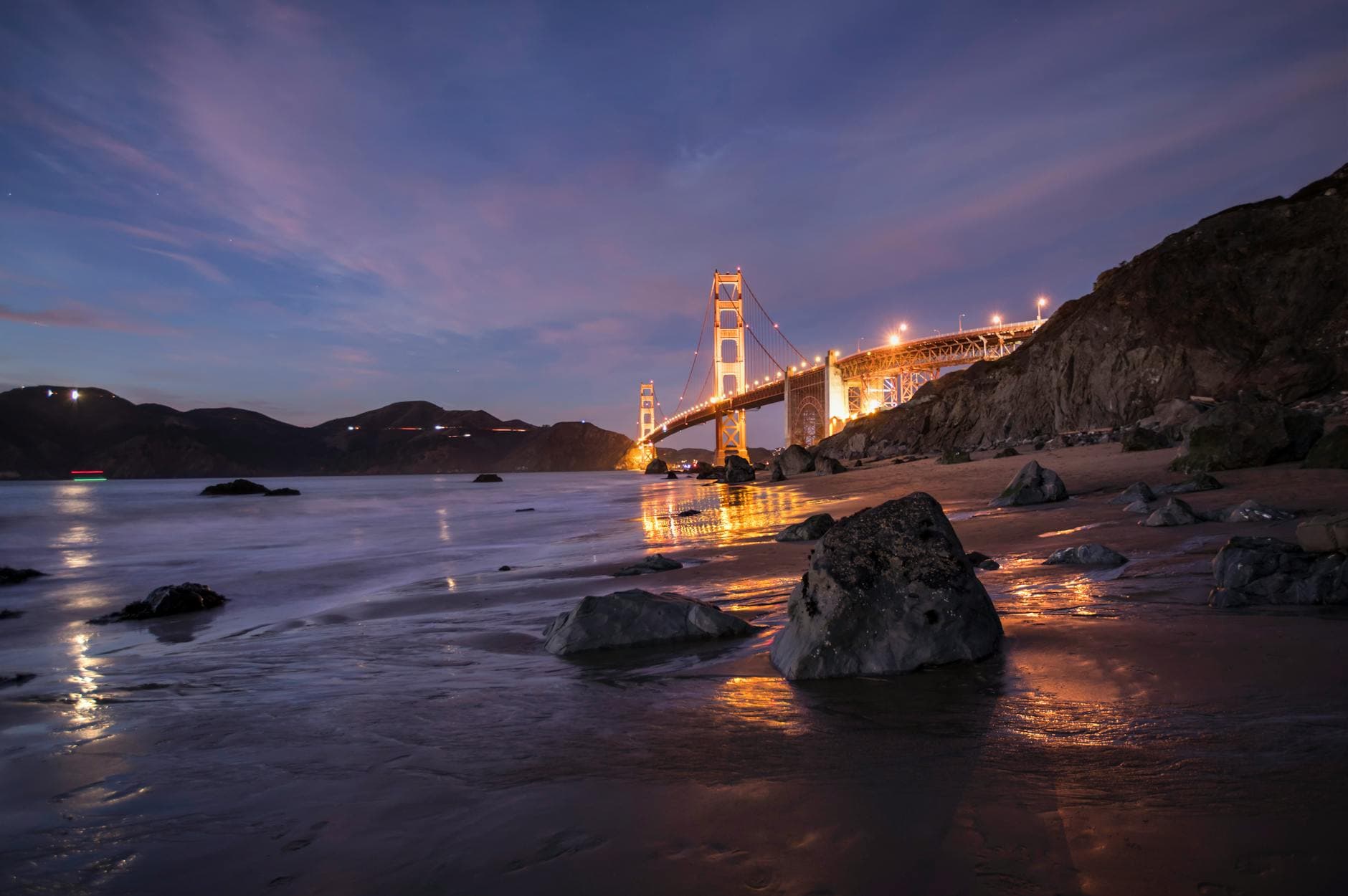 Stunning view of Golden Gate Bridge at twilight, reflecting on a serene beach in San Francisco.