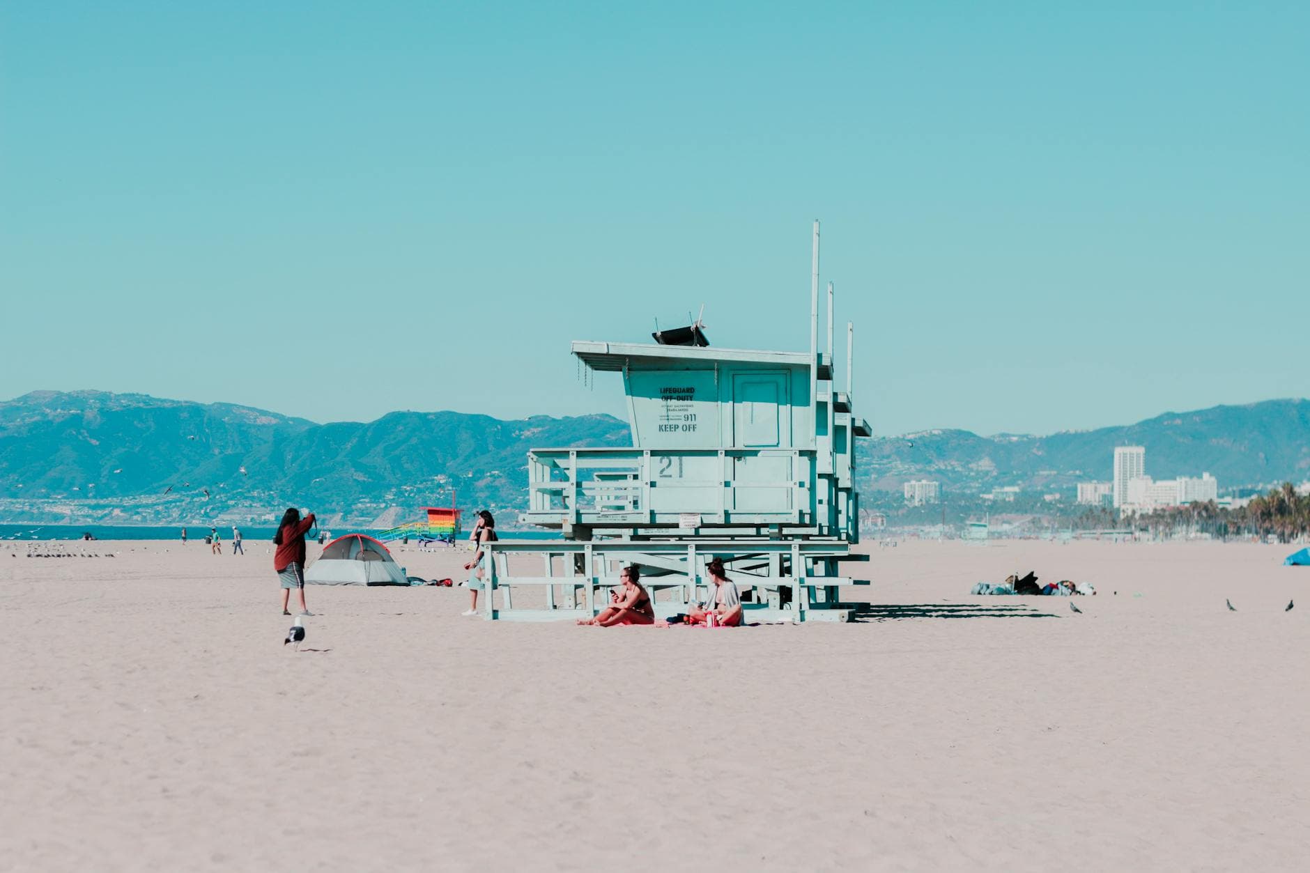 Sunny day at Santa Monica Beach featuring a lifeguard tower and beachgoers with a mountain view.