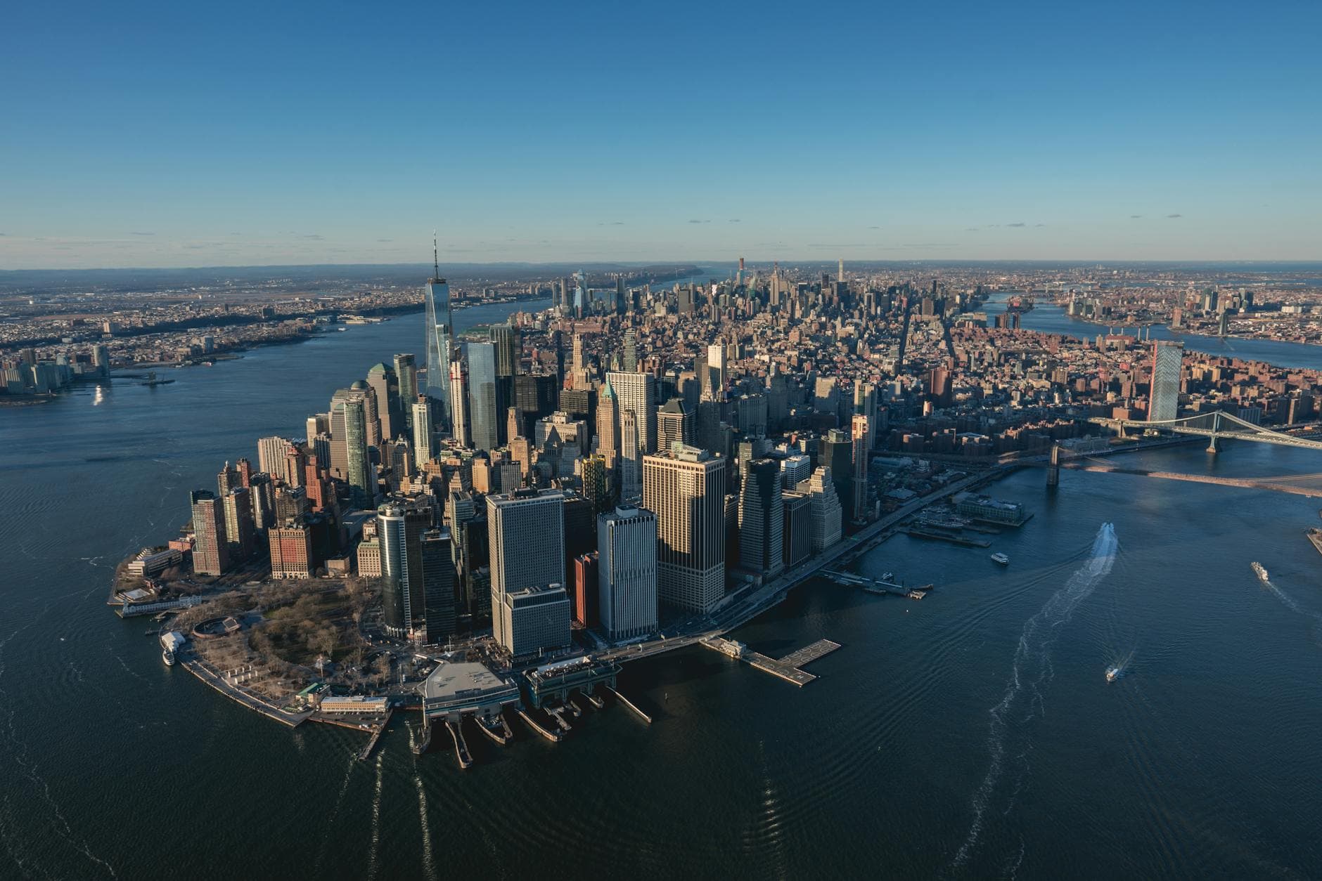 Aerial view of New York City's Lower Manhattan skyline with rivers and bridges visible.