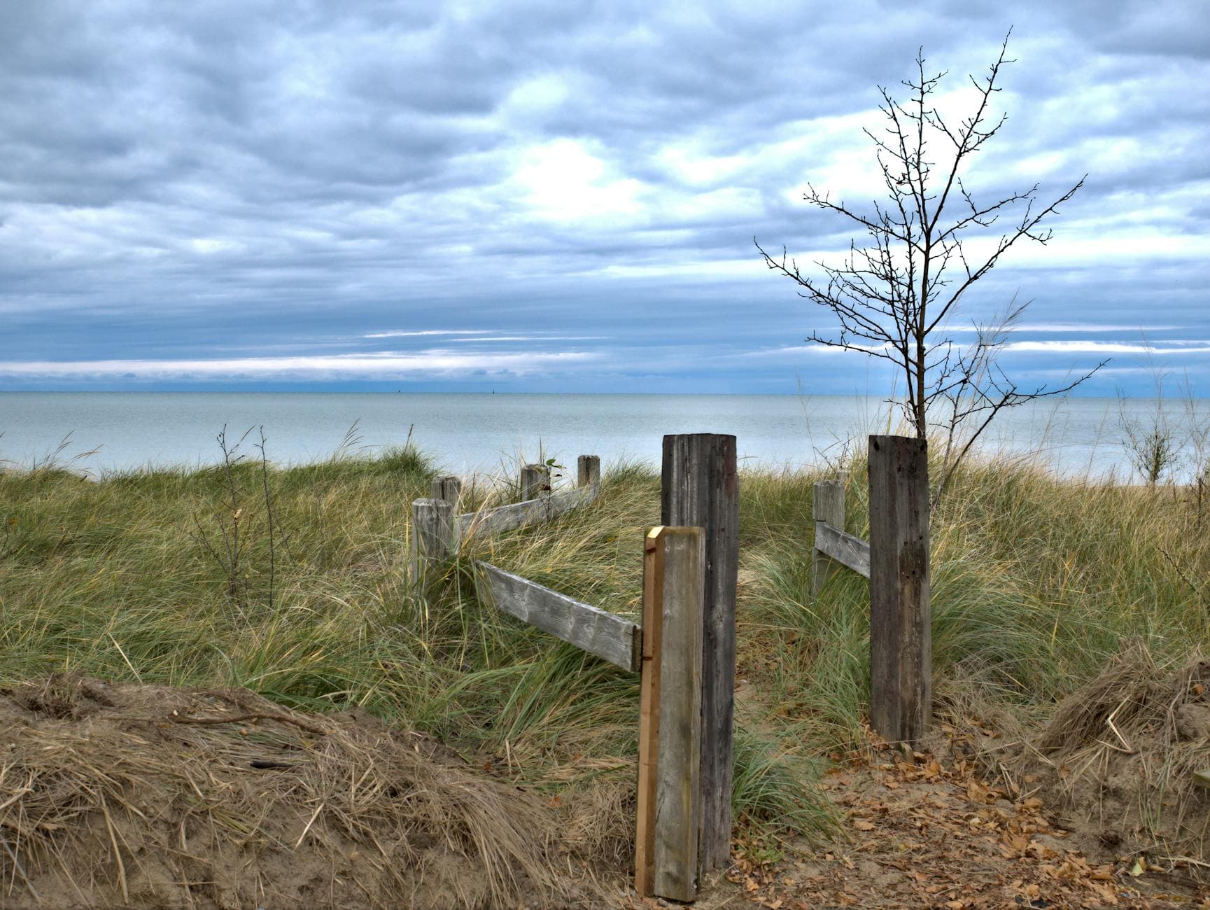 A peaceful view of a beach with wooden fence and grass under a cloudy sky in Southampton, Ontario, Canada.