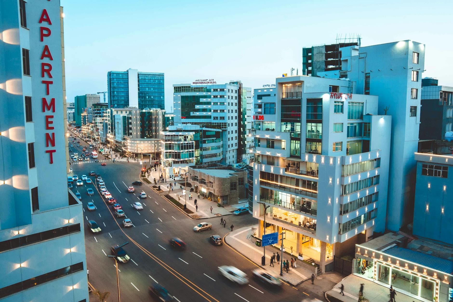 A bustling street scene in Addis Ababa with modern architecture, traffic, and city lights at twilight.