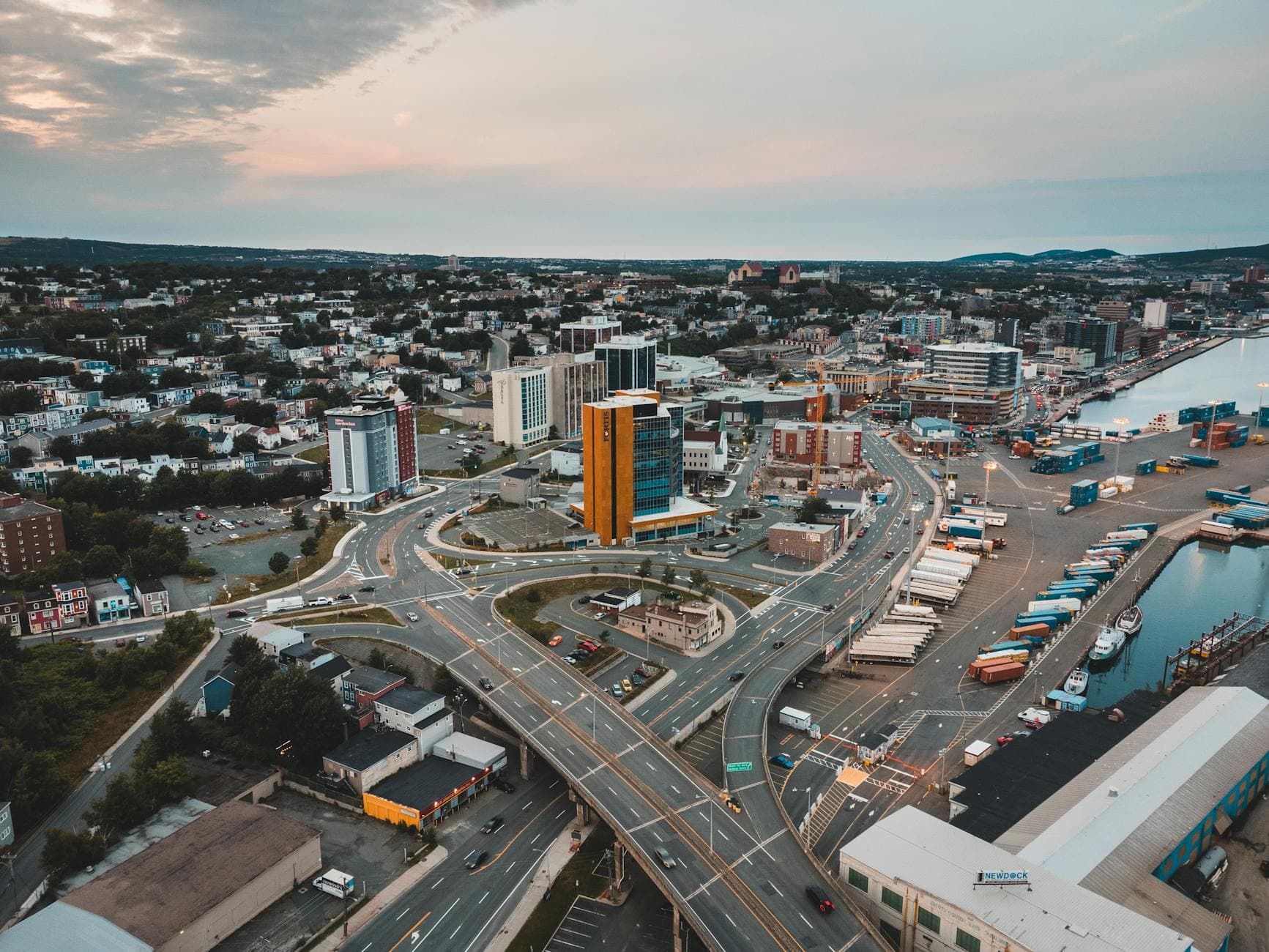 Dynamic aerial view of a cityscape featuring highways, buildings, and waterfront at sunset.