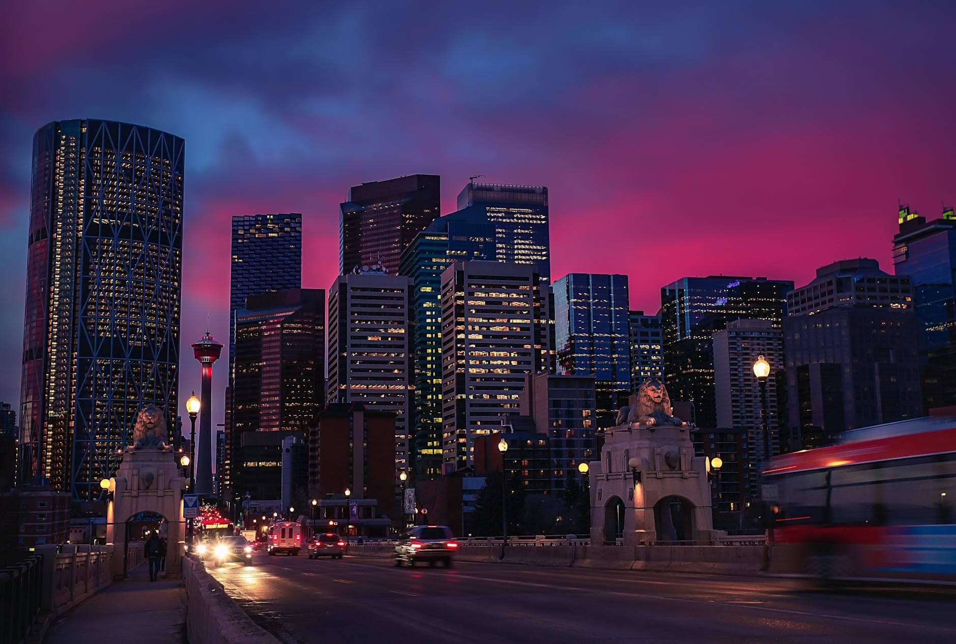 Stunning view of Calgary's illuminated skyline during a vibrant pink sunset, featuring skyscrapers and urban landscape.