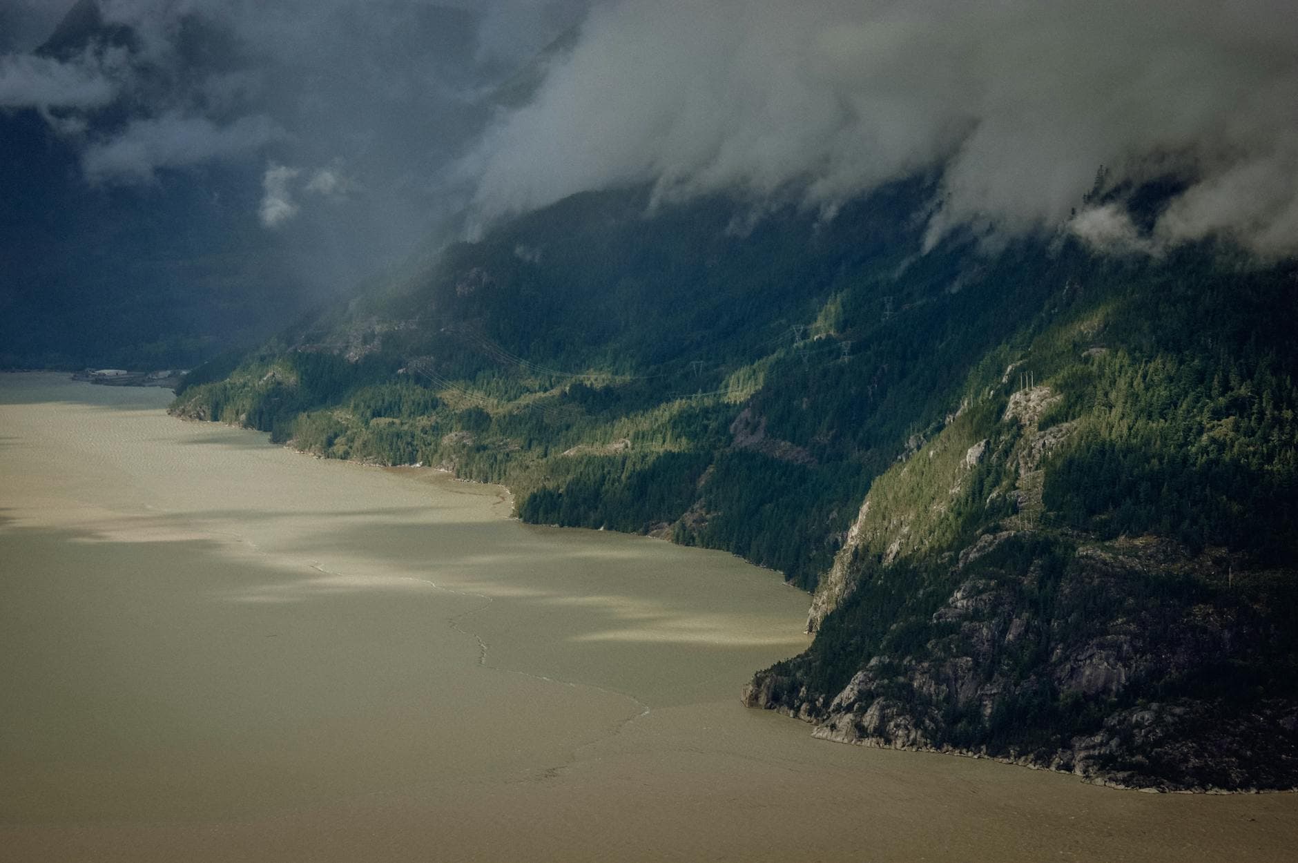 Aerial view of the misty coastline near Squamish, BC, Canada, with lush forests and dramatic cloud cover.