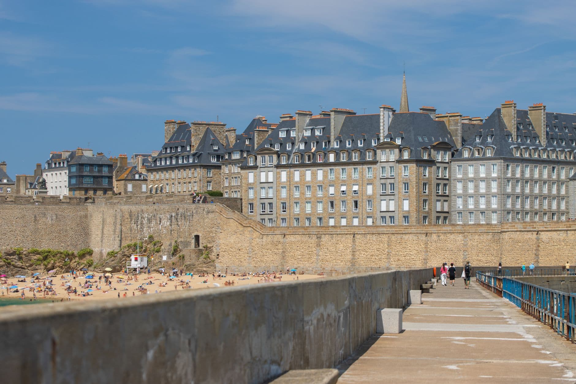 Tourists enjoy the sunny day at Saint-Malo beach with historic city walls in the background, showcasing Brittany's charm.