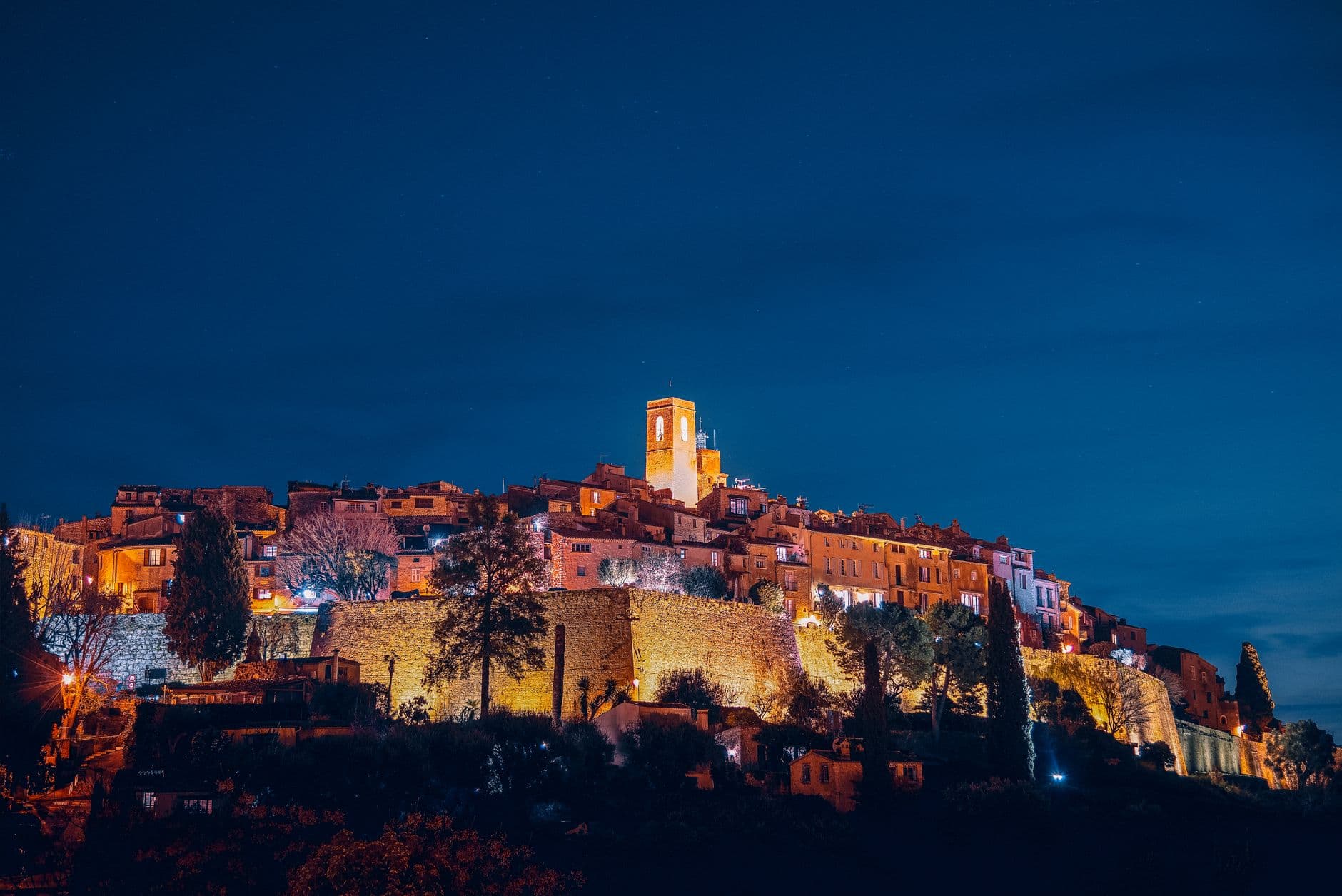 From below of amazing aged Saint Paul de Vence commune with illuminated buildings and ancient bell tower located on hill against evening sky
