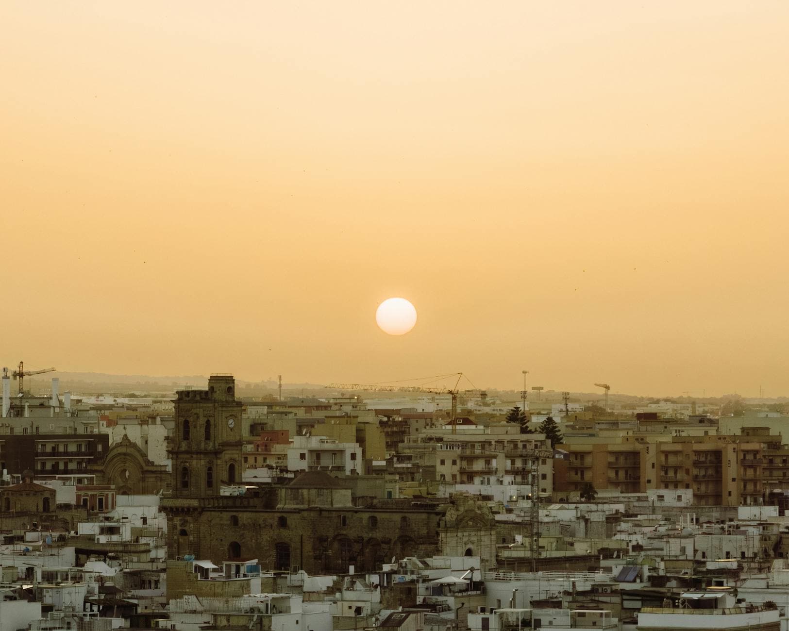 Aerial view of the cityscape of Monopoli, Italy at sunset, highlighting historic architecture and a tranquil yellow sky.