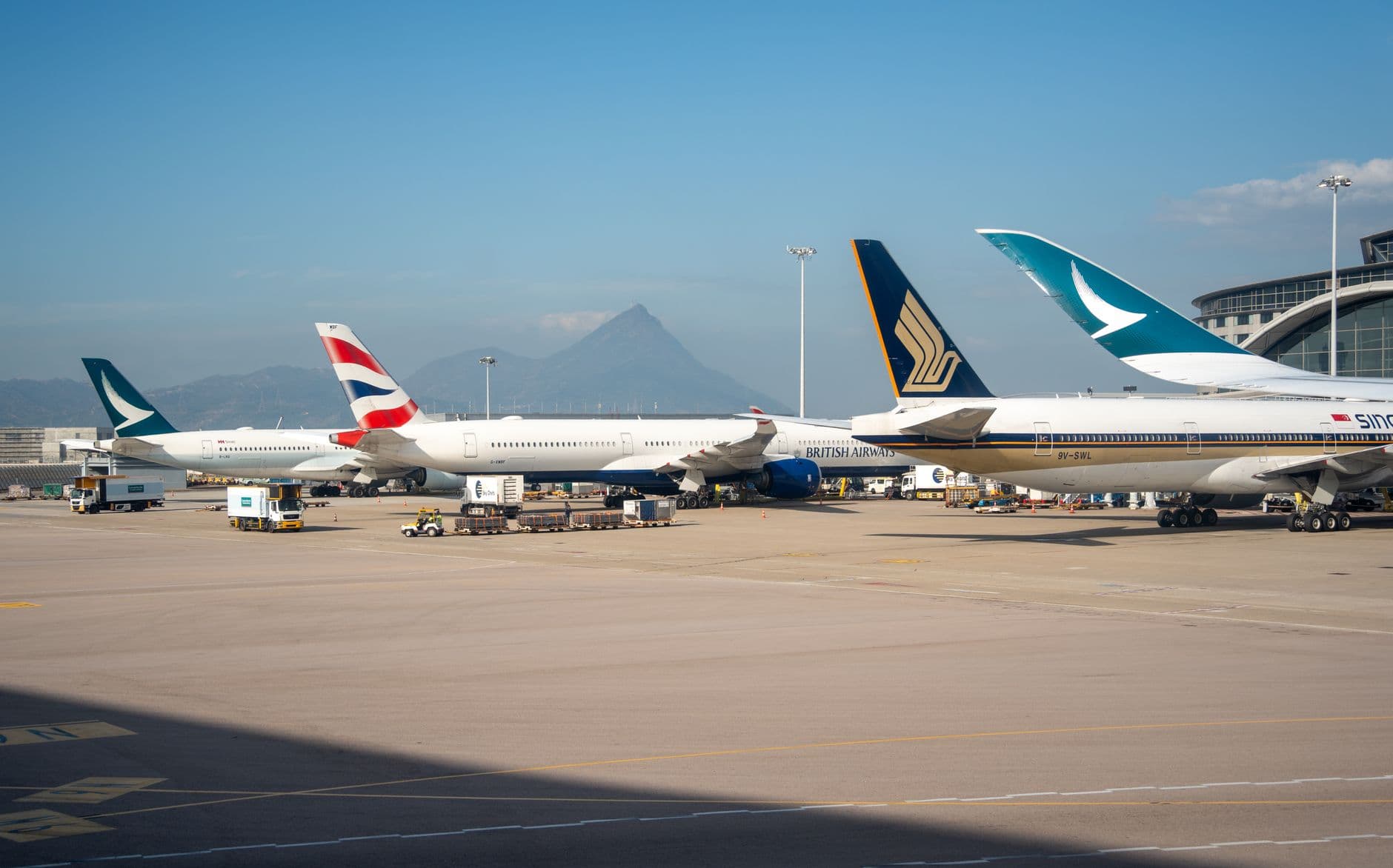 Multiple commercial airplanes parked at an airport terminal with a mountain view in the background.