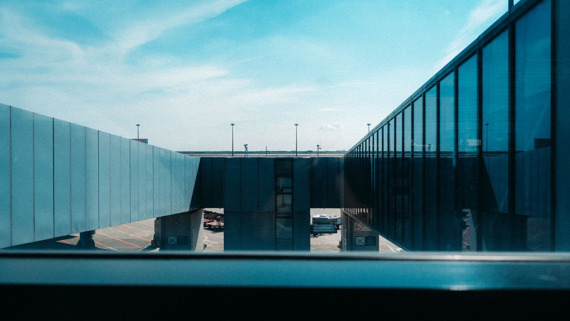 A view of a sleek airport skybridge with blue reflective glass under a clear sky.