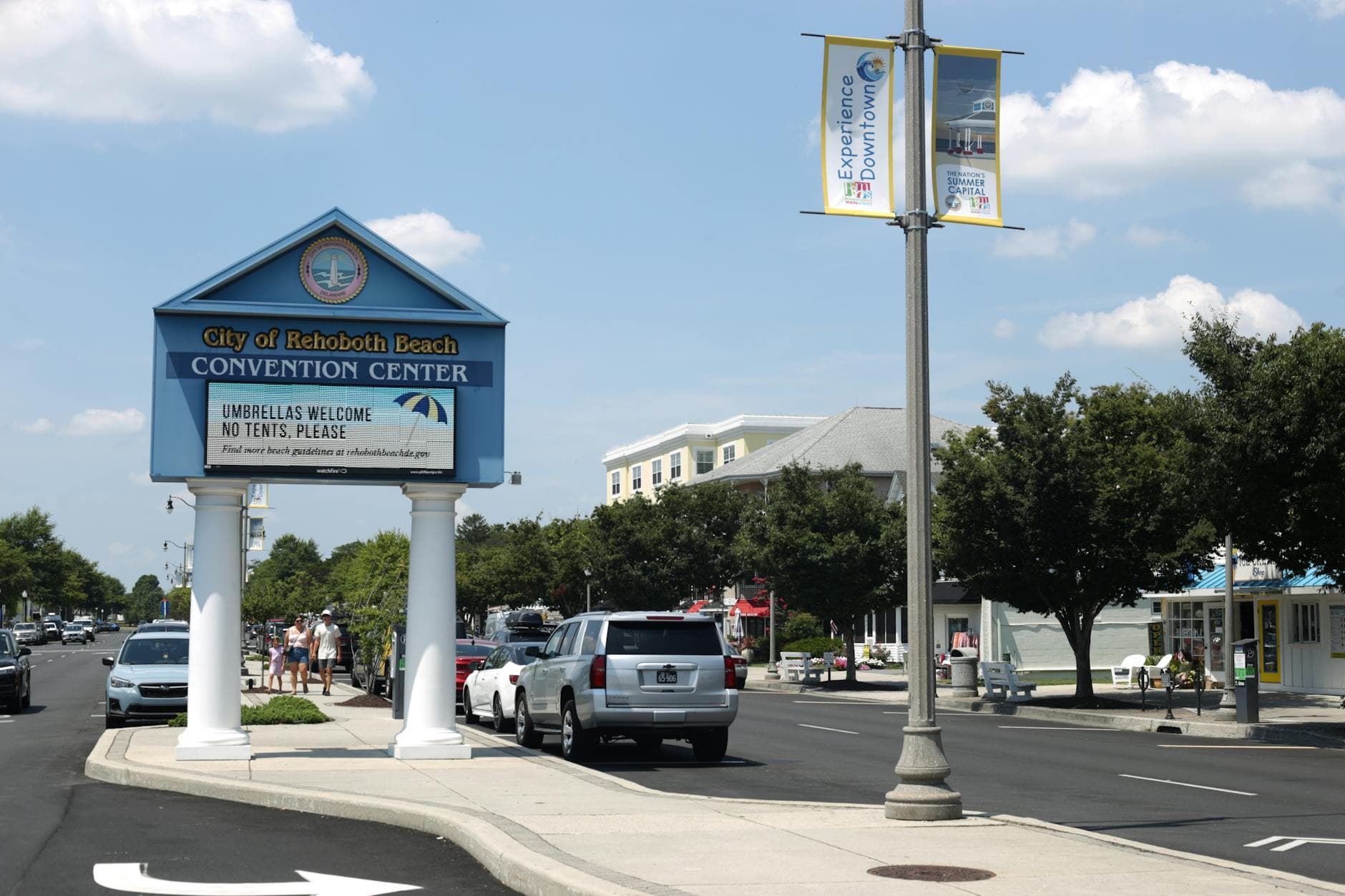 Street view of City of Rehoboth Beach Convention Center with cars and people on a sunny day.