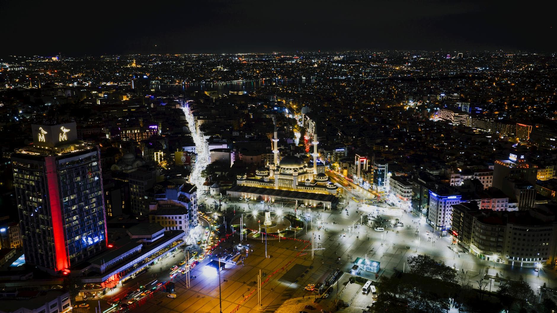 A stunning aerial night view of Taksim Square, Istanbul, illuminated and bustling with city lights.