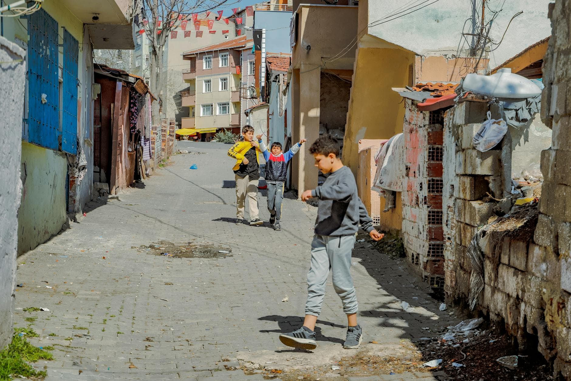 Children playing on a sunlit street in Tekirdağ city, Türkiye, showcasing urban life.