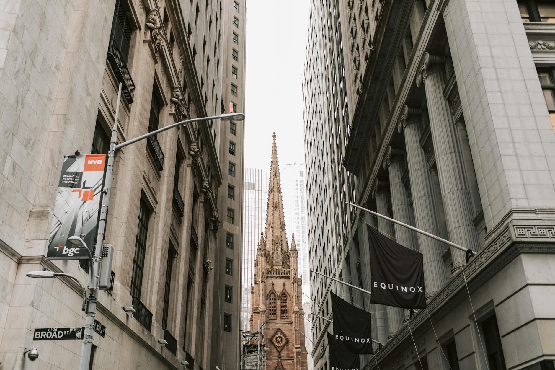 View of Trinity Church between skyscrapers on Broad Street, NYC, showcasing historic architecture.