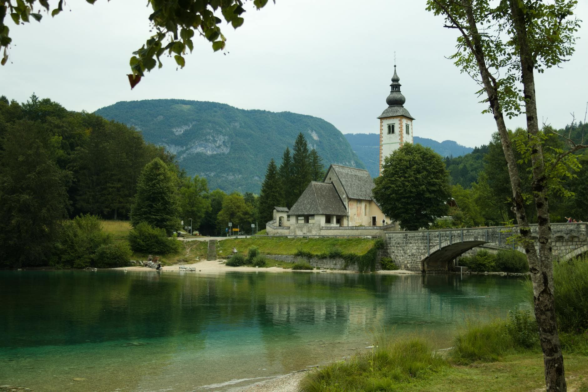 Beautiful view of a historic church and bridge in Bohinjska Bistrica, Slovenia, surrounded by nature.