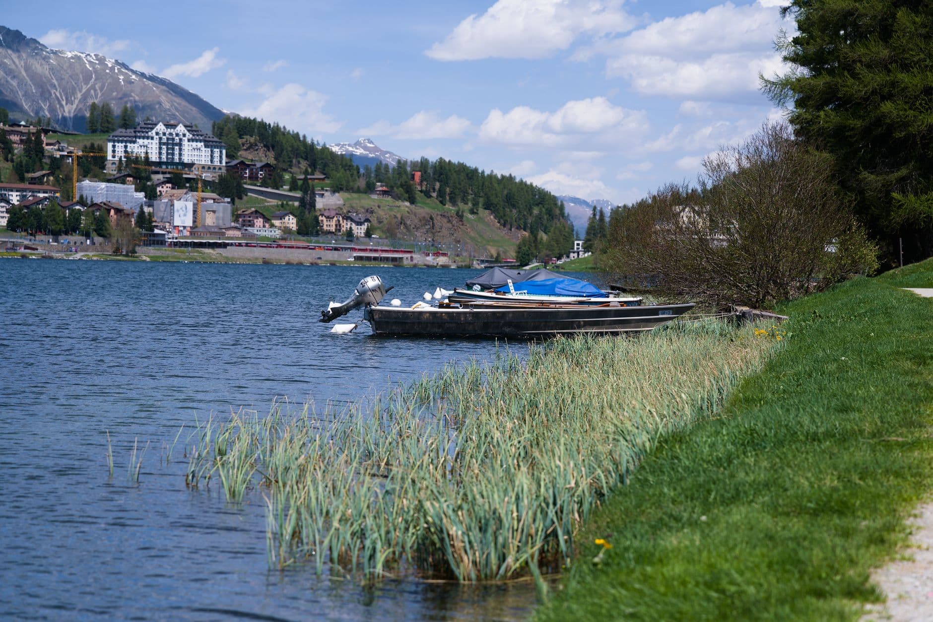 Beautiful landscape of Lake St. Moritz, showcasing boats by the shore with snow-capped mountains in the background.