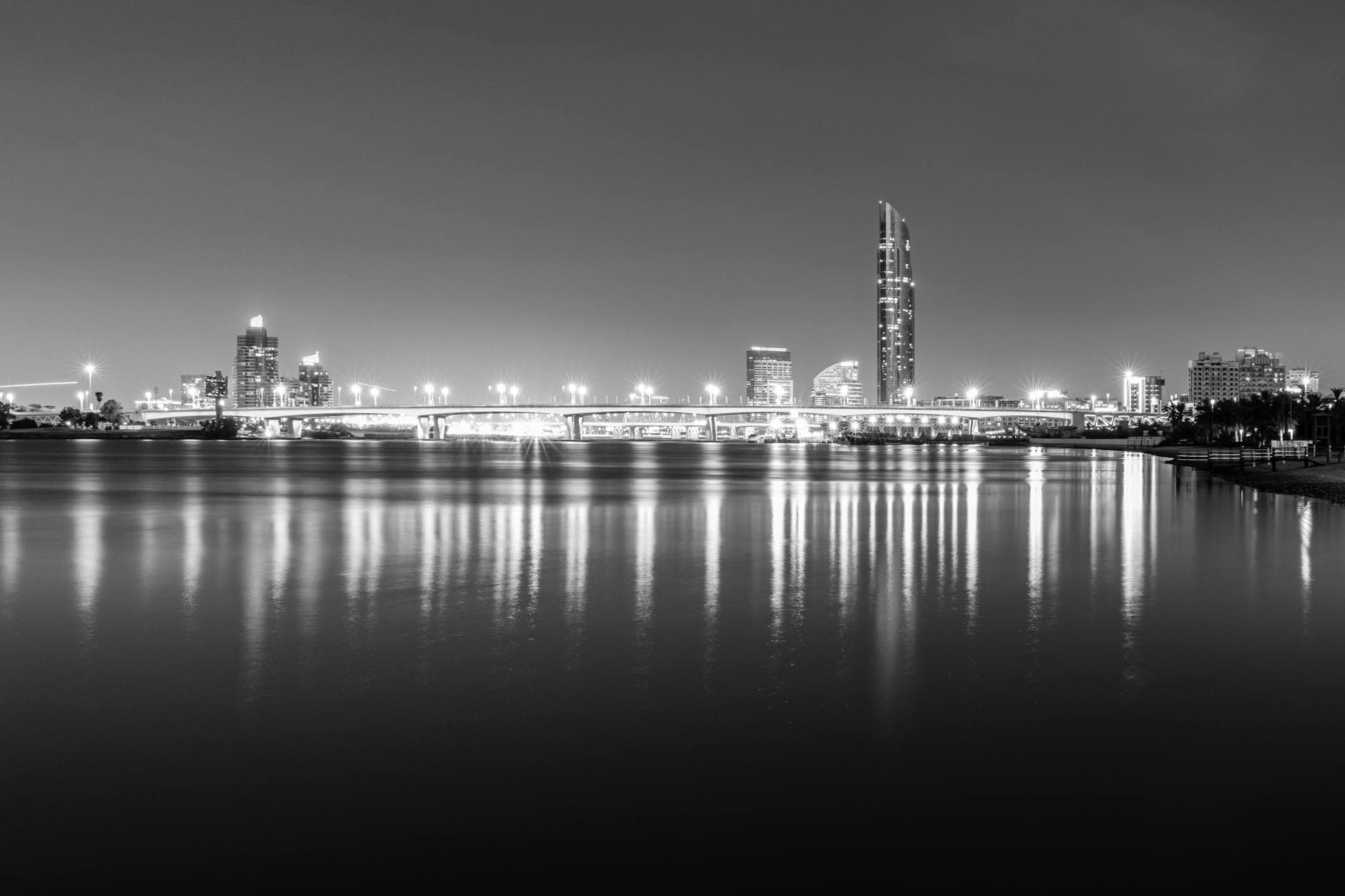Black and white photo of Dubai skyline at night with reflections on the creek.
