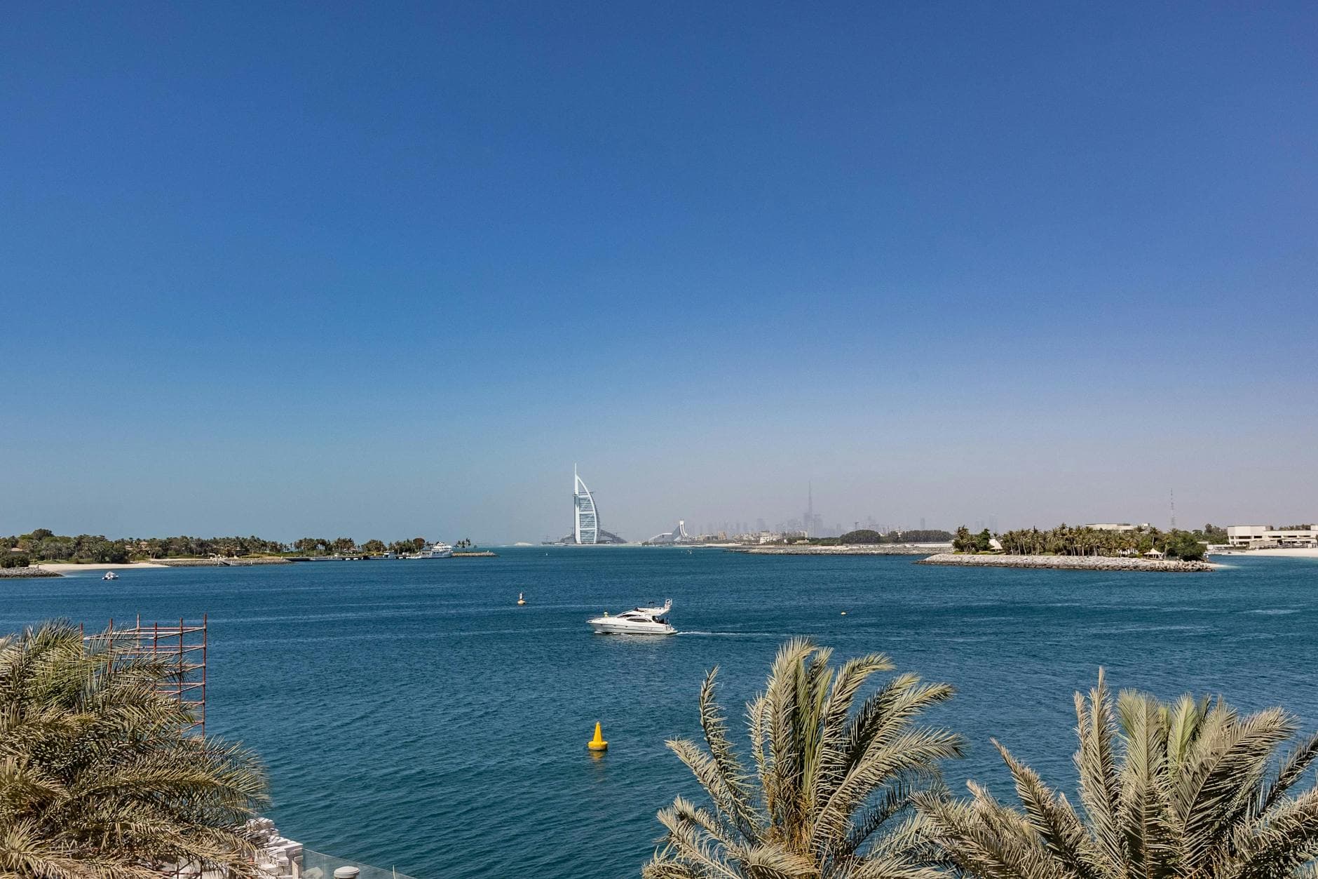 Breathtaking view of the Burj Al Arab from Dubai's coastline featuring serene waters and palm trees.