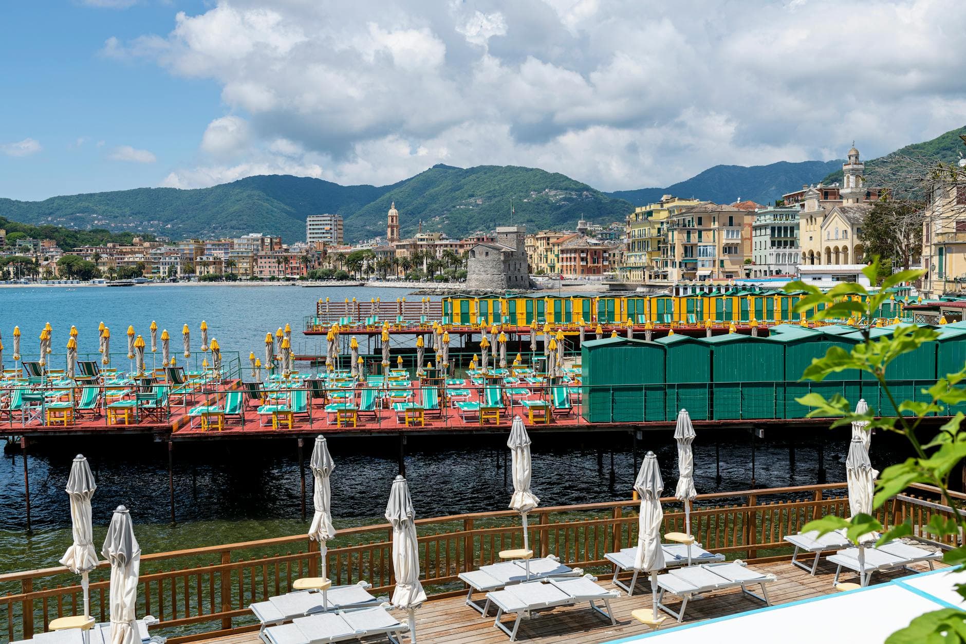 Vibrant beachside with umbrellas and cityscape in Rapallo, Liguria, Italy under a clear sky.