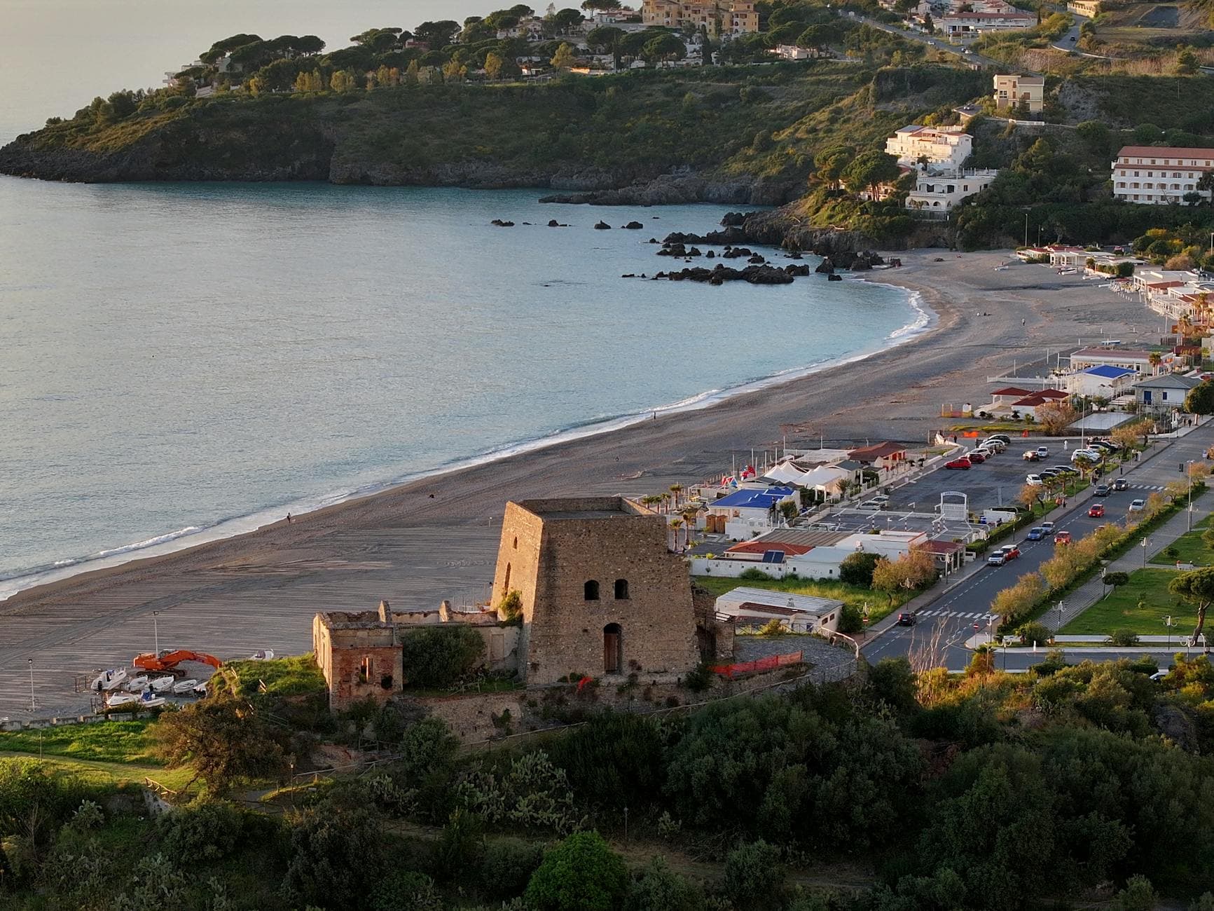 Aerial view of a coastal beach and historic ruins at sunset, featuring stunning natural beauty.
