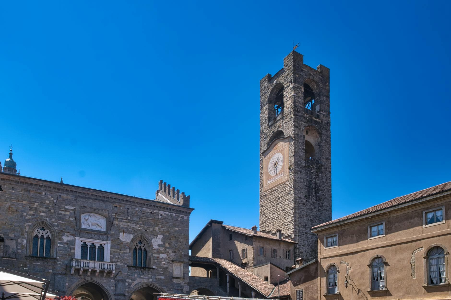 View of the historical Torre Civica and medieval architecture in Bergamo, Lombardy, under a clear blue sky.