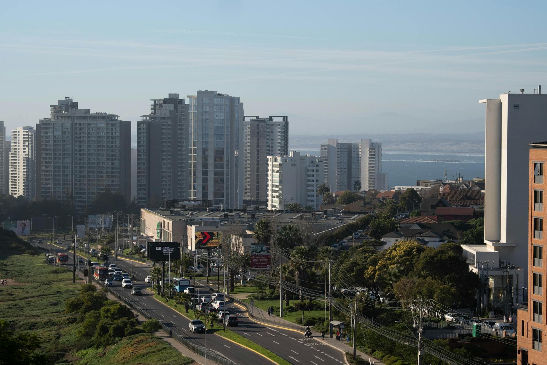 Aerial city view featuring tall buildings and a distant coastline under a clear blue sky.