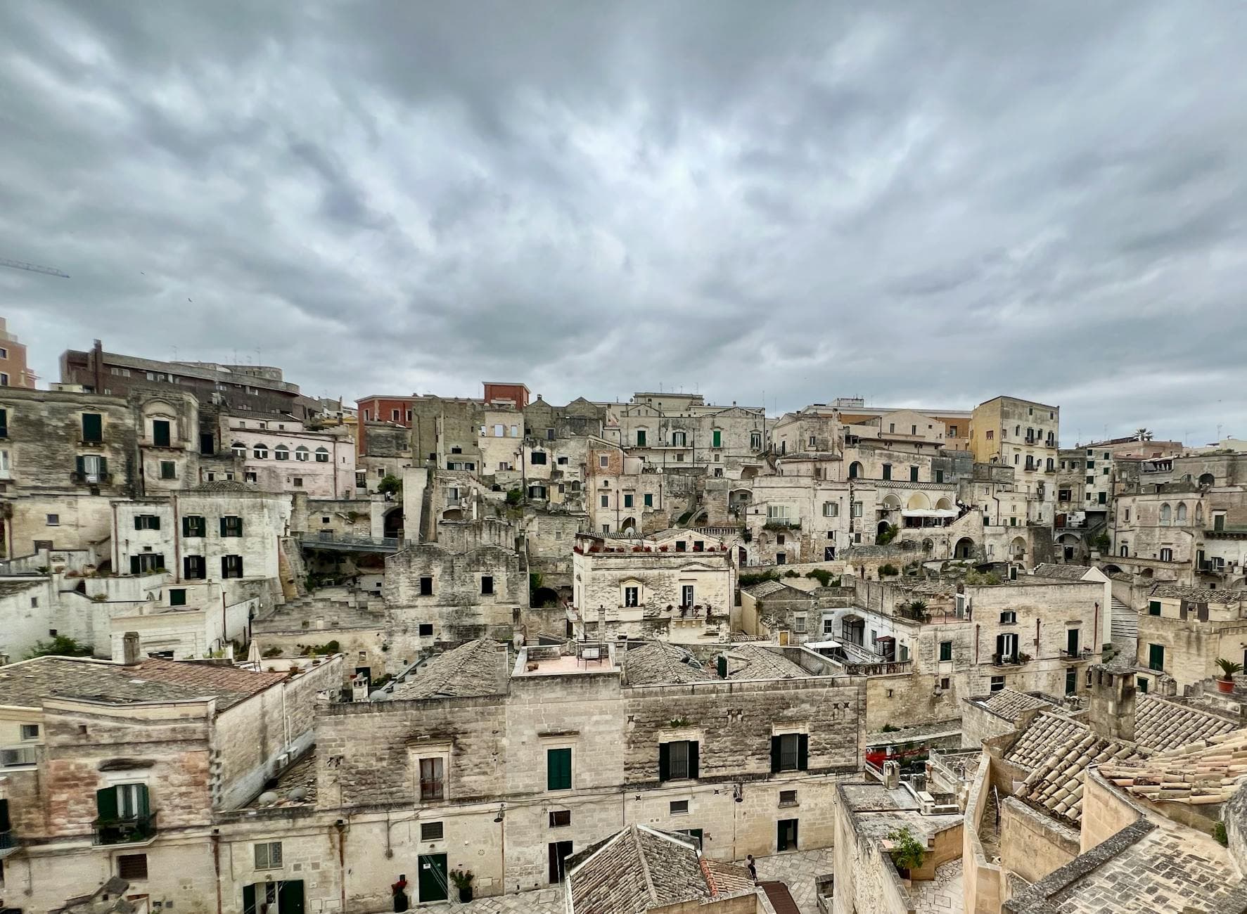 Aerial view of Matera's historic stone dwellings and rooftops under a dramatic cloudy sky.