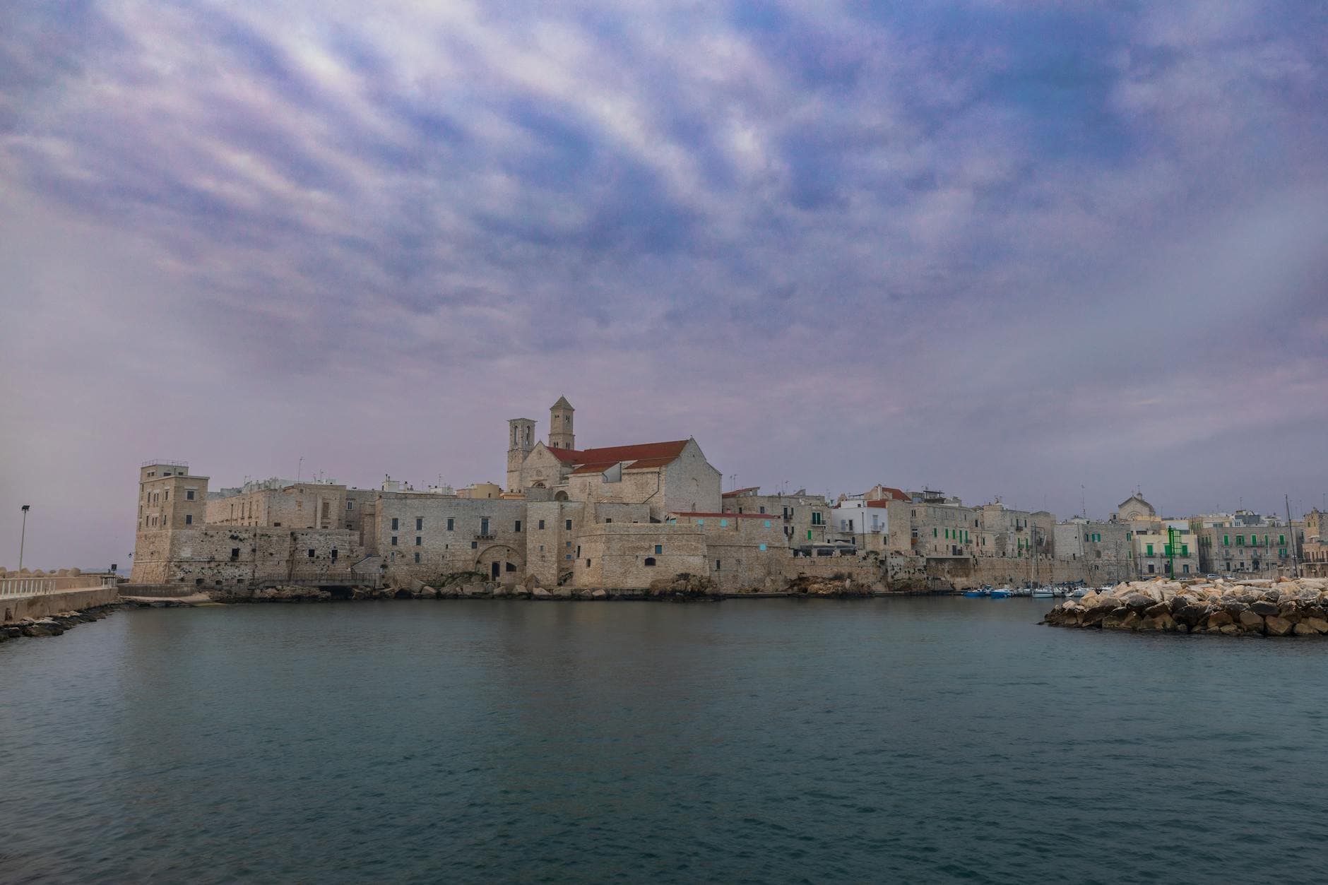 Scenic view of a historic Italian coastal town with stone buildings and calm water under a vibrant sky.
