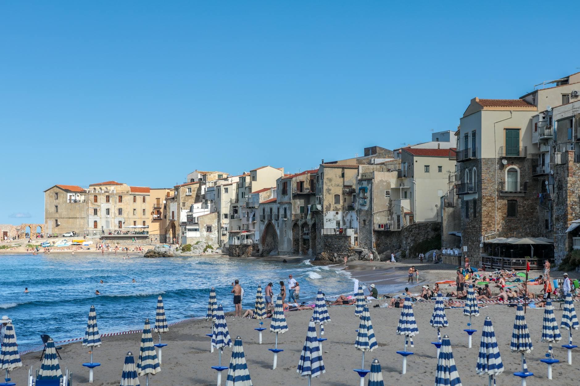 Picturesque beach with umbrellas in a historic village on Sicily's coast, ideal for travel content.
