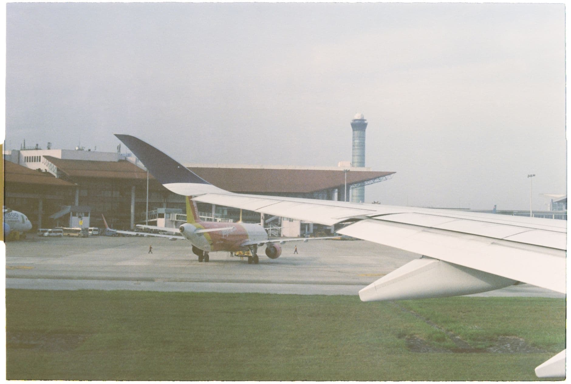 View of an airport terminal with planes on the runway, a control tower visible.