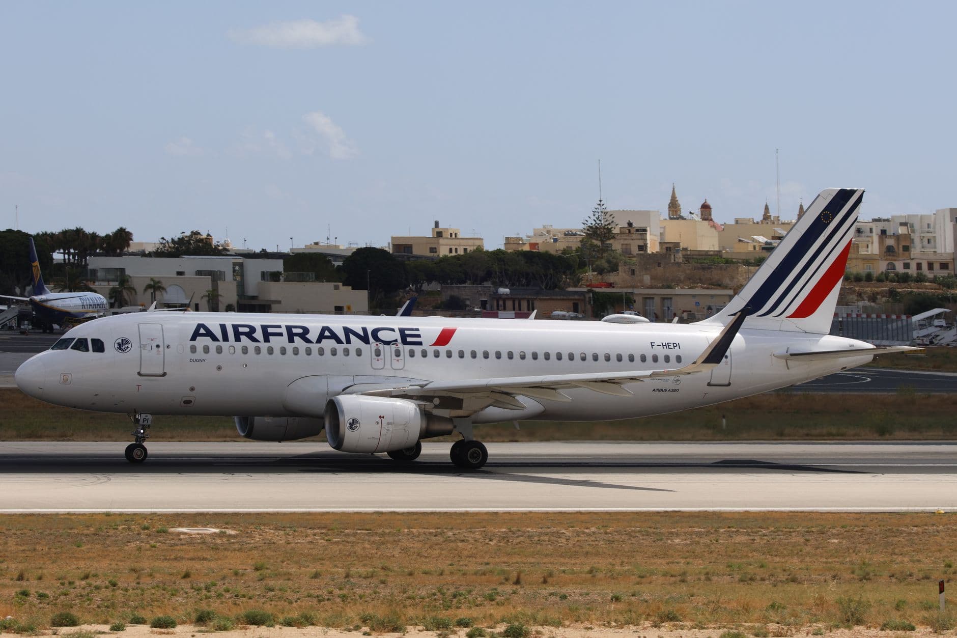 Air France Airbus A319 taxiing on a sunny runway with a cityscape backdrop.