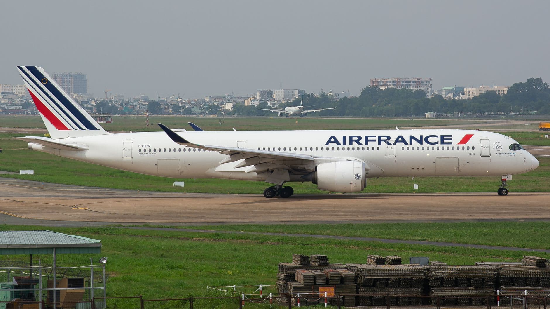 Side view of Air France Airbus A350 taxiing on a runway, cityscape in background.