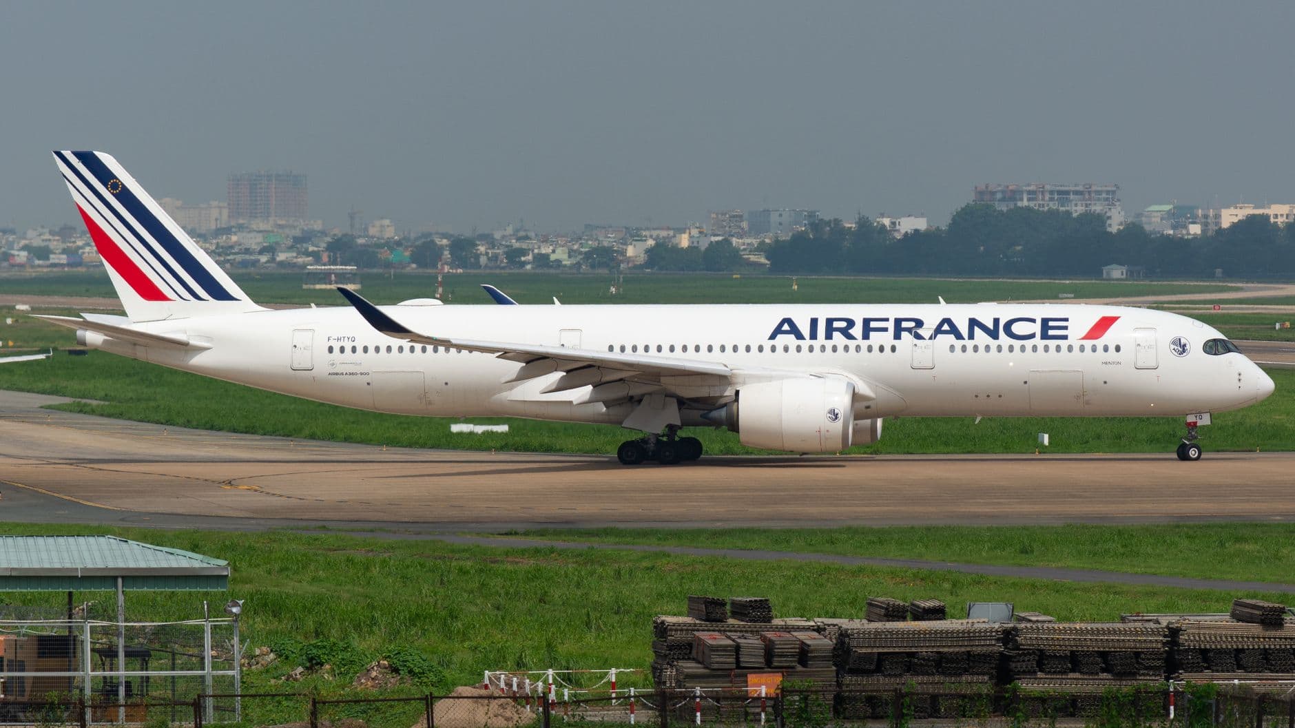 Air France Airbus A350 aircraft taxies on airport runway with cityscape backdrop.