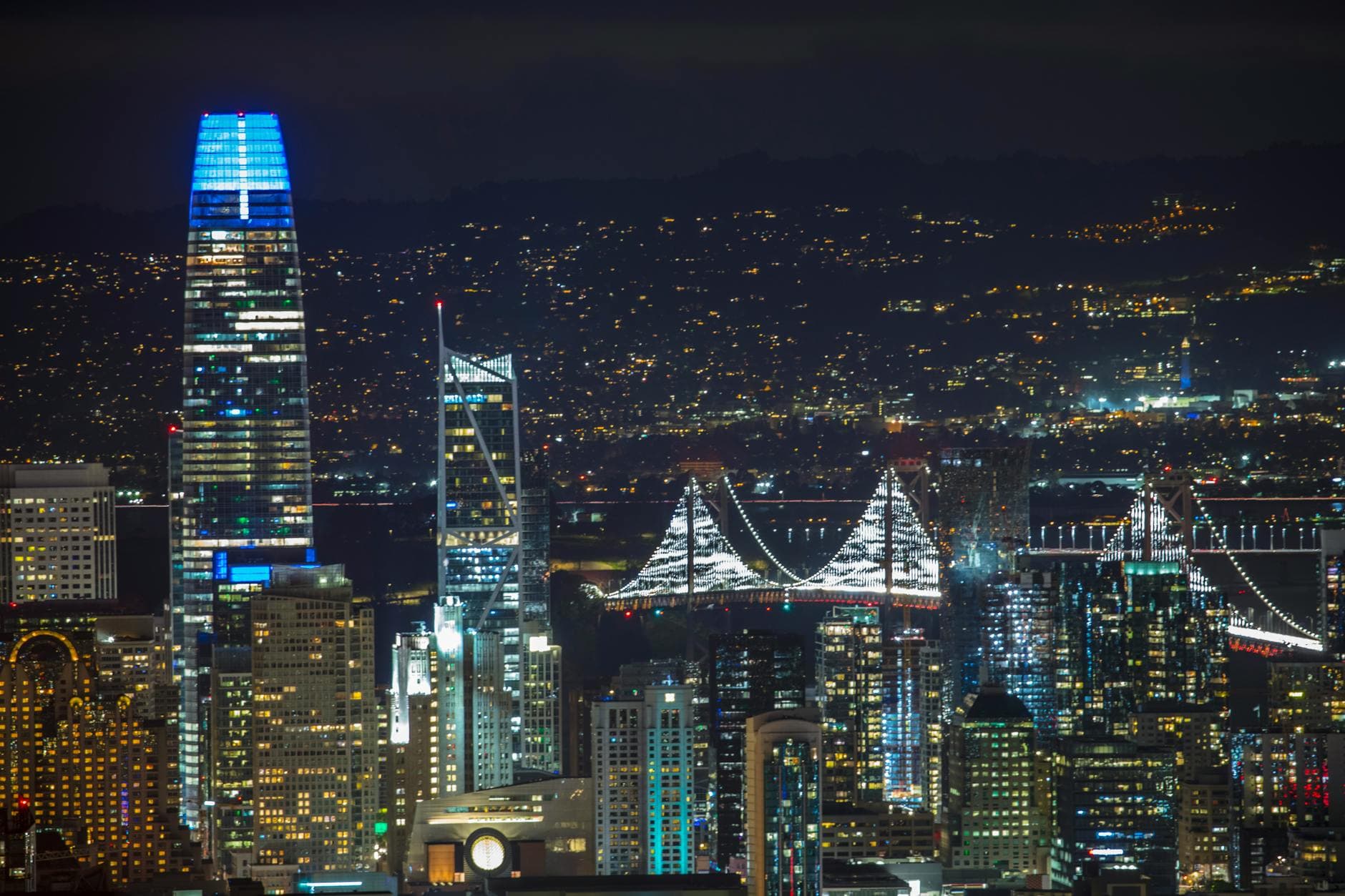 A vibrant night view of San Francisco's skyline featuring the illuminated Bay Bridge and skyscrapers.