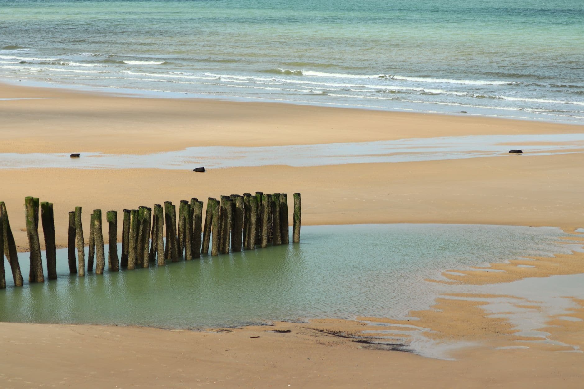 A peaceful beach with wooden groynes and waves in Wissant, France.