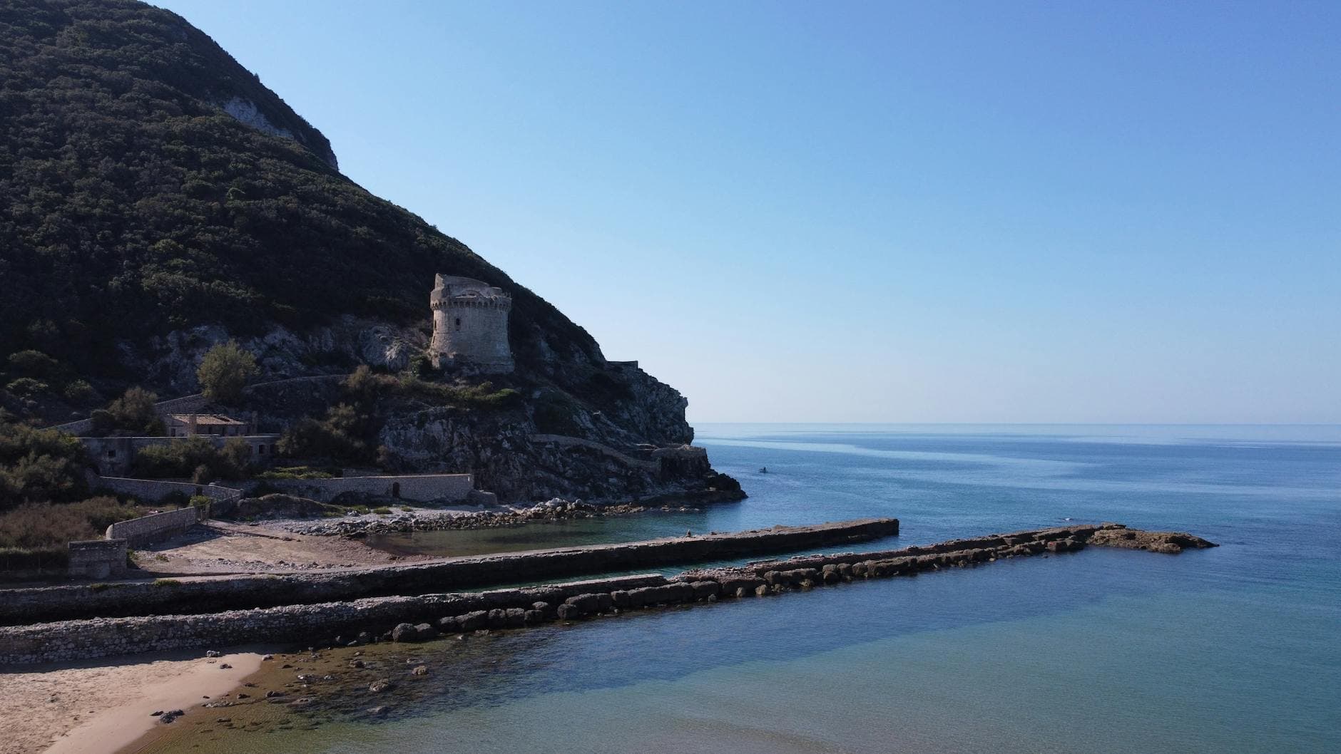 Breathtaking view of Anzio's coastline featuring a historic tower and breakwater under a clear blue sky.