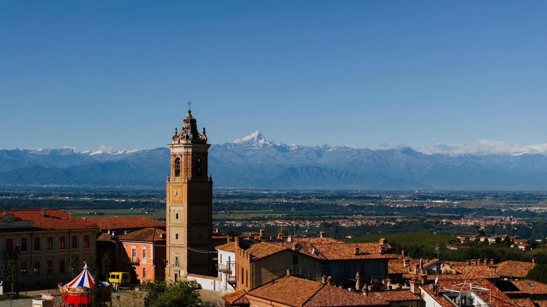 A historic bell tower rises above the charming town of La Morra in Italy, amidst stunning mountain views.