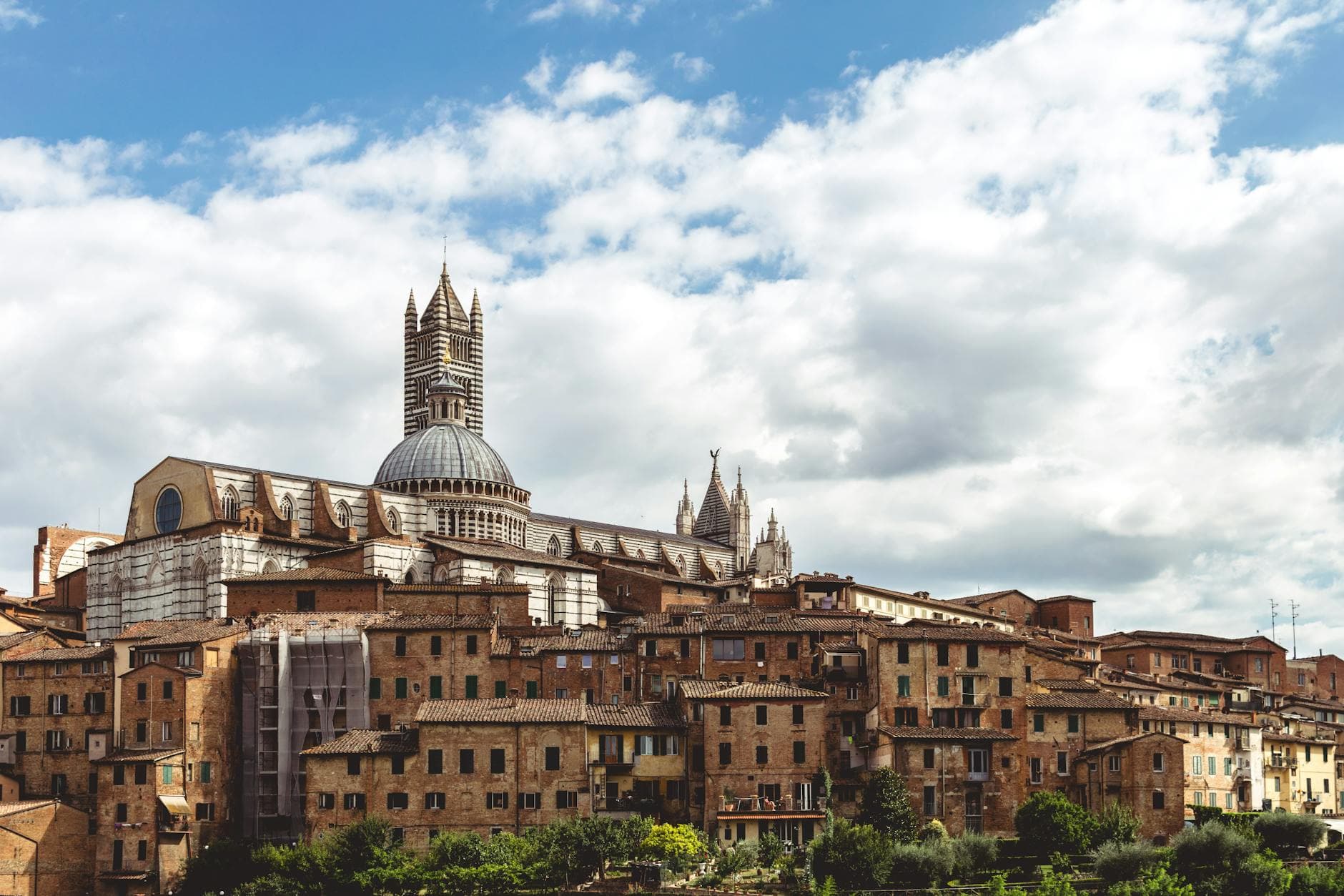A scenic view of Siena's historic cityscape featuring the iconic Siena Cathedral under a cloudy sky in Tuscany, Italy.