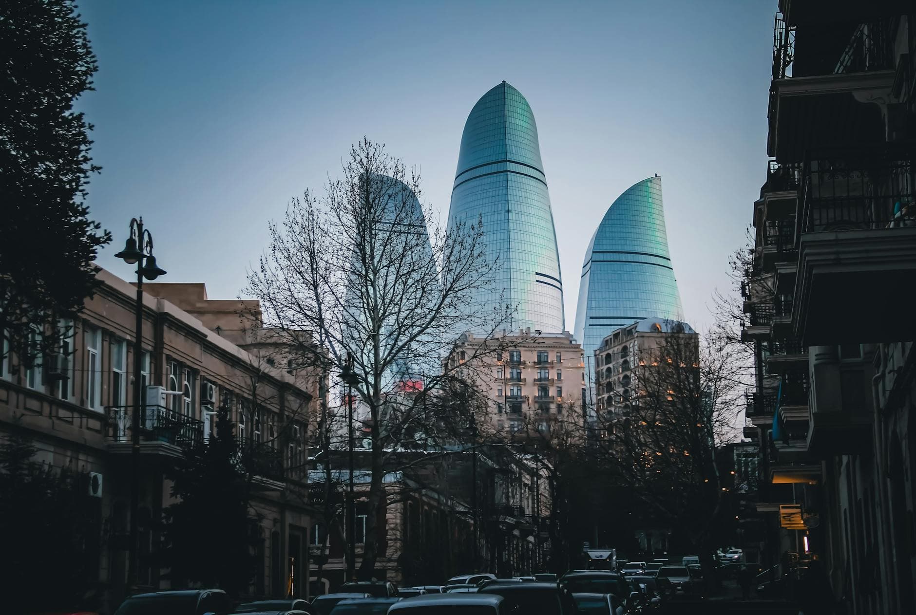 Evening view of Baku's iconic Flame Towers amidst urban cityscape and bare trees.