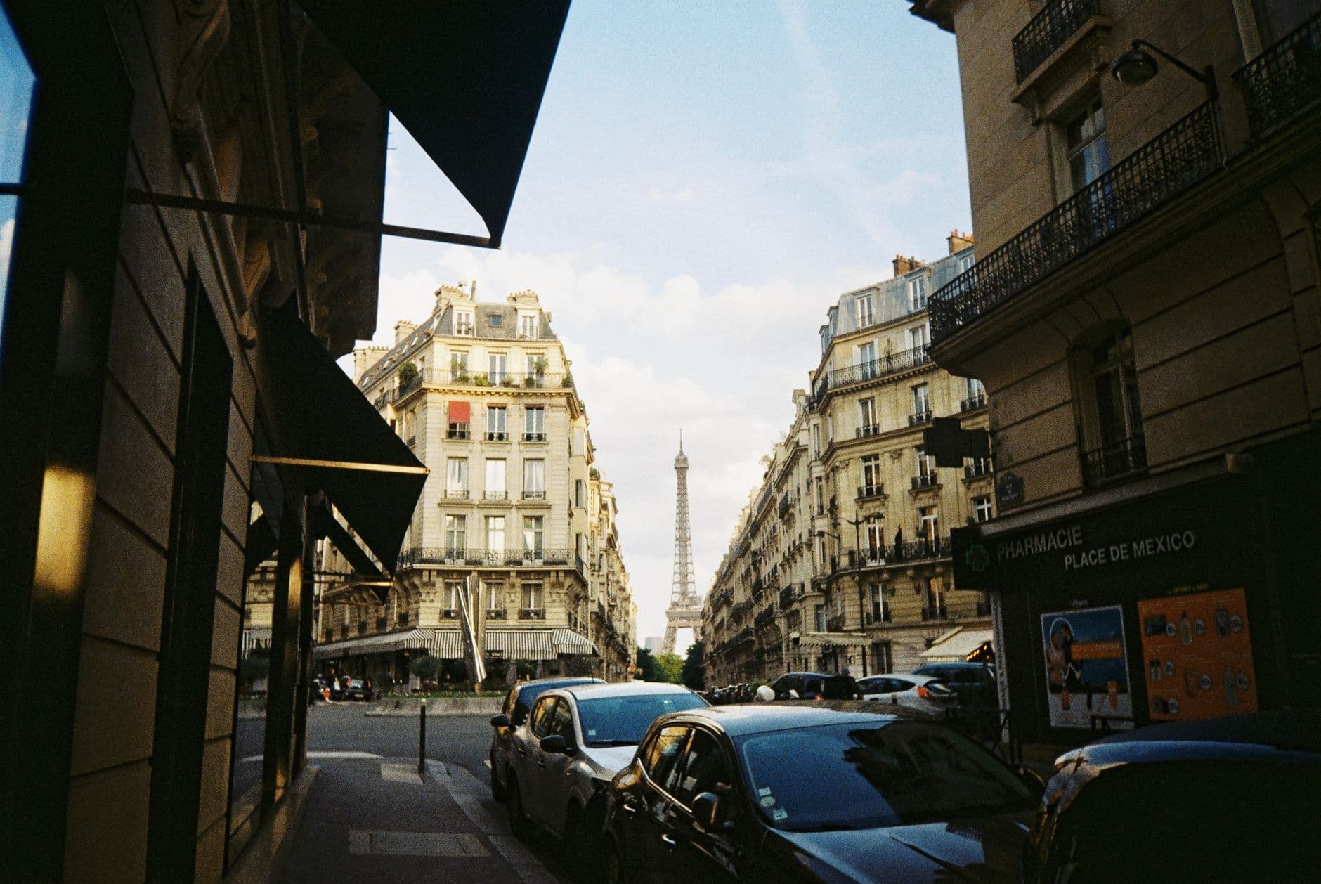 A classic Paris cityscape featuring the Eiffel Tower framed by elegant Haussmann buildings in a busy street.