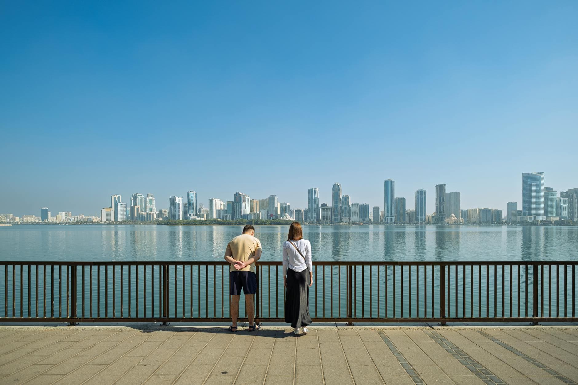 A couple stands by the waterfront, admiring the modern skyline of Sharjah, United Arab Emirates.