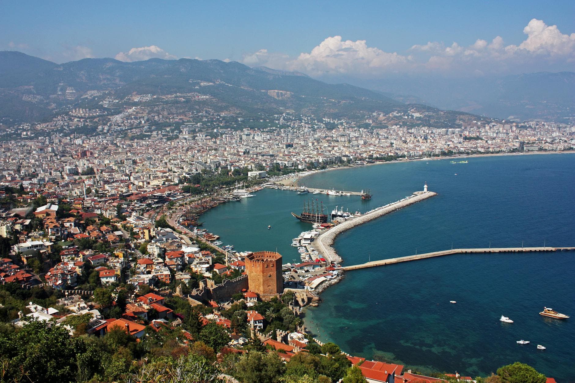 Aerial view of Antalya's harbor and cityscape with clear blue sea and historic sites.