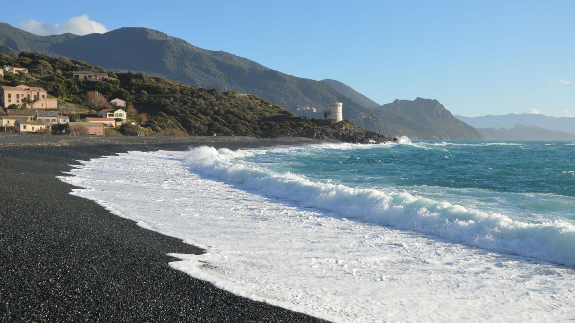 Beautiful coastal landscape with waves crashing on Ogliastro beach, Corse, France, under a clear blue sky.